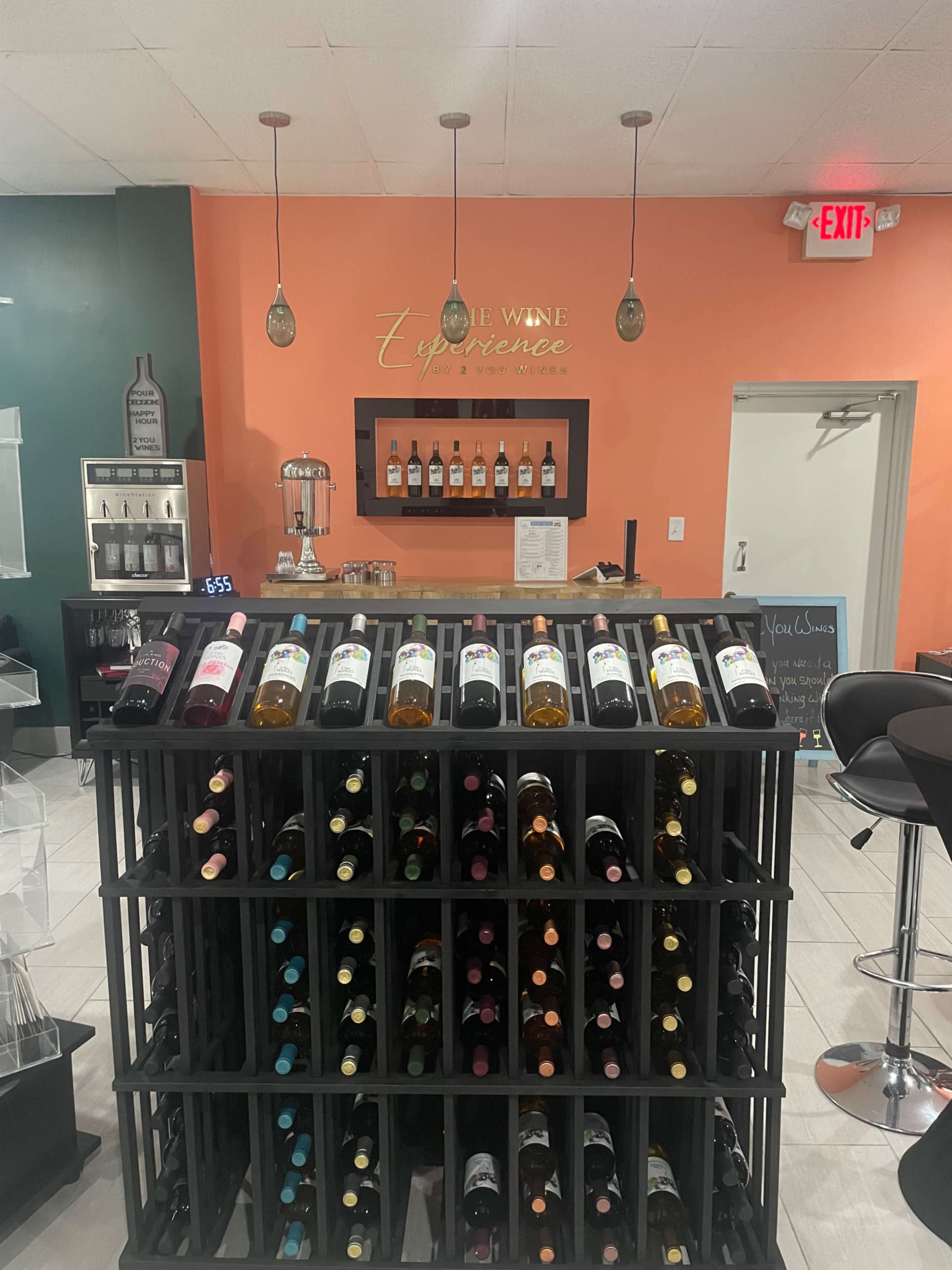 The image shows a wine shop featuring a display rack filled with various wine bottles and a backdrop with a counter where several wine bottles are arranged.
