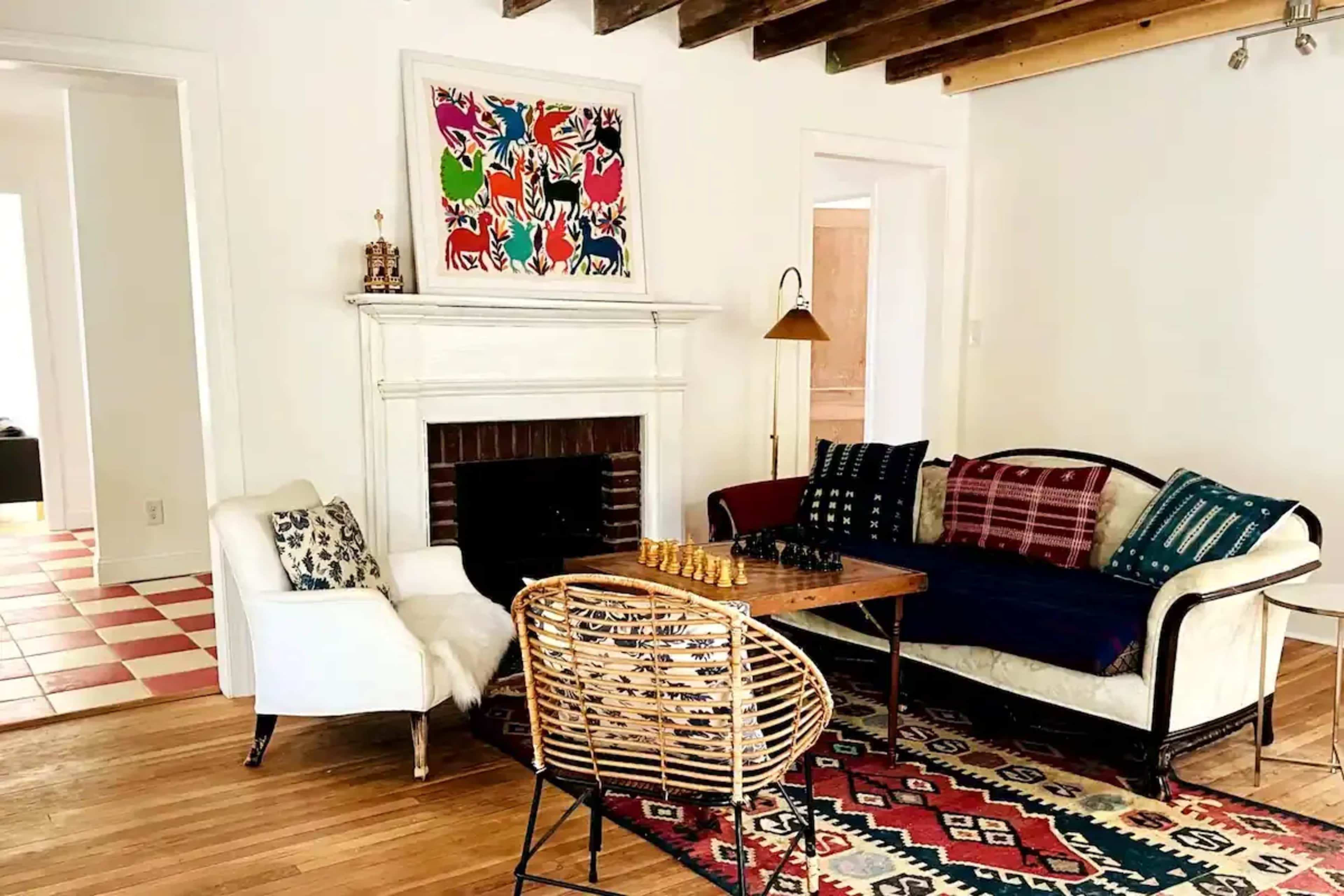A living room with a fireplace, a chess table with pieces, a sofa, and patterned rugs.