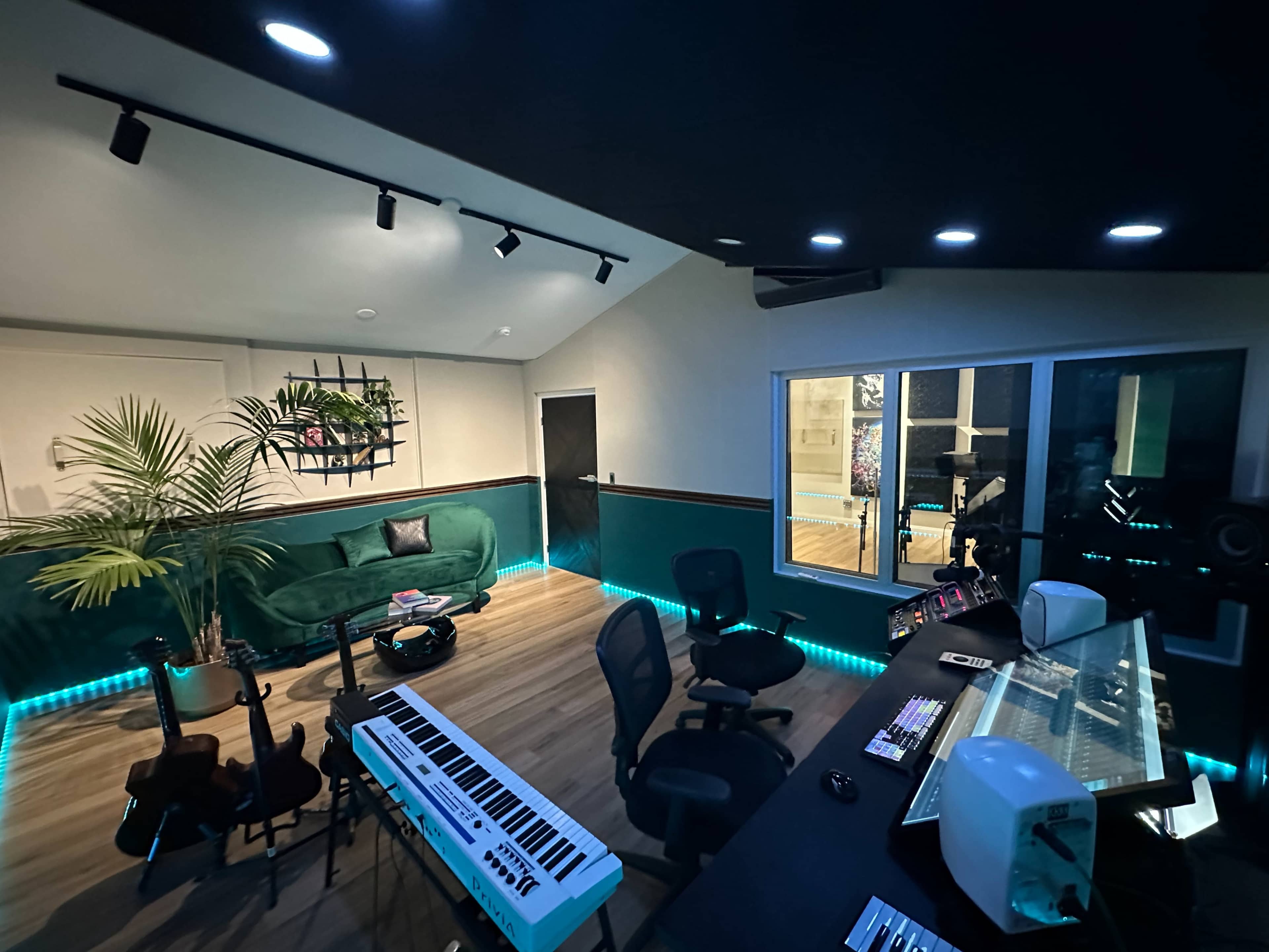 A modern music studio with a mixing desk, musical instruments, a green couch, and lighting along the floor.