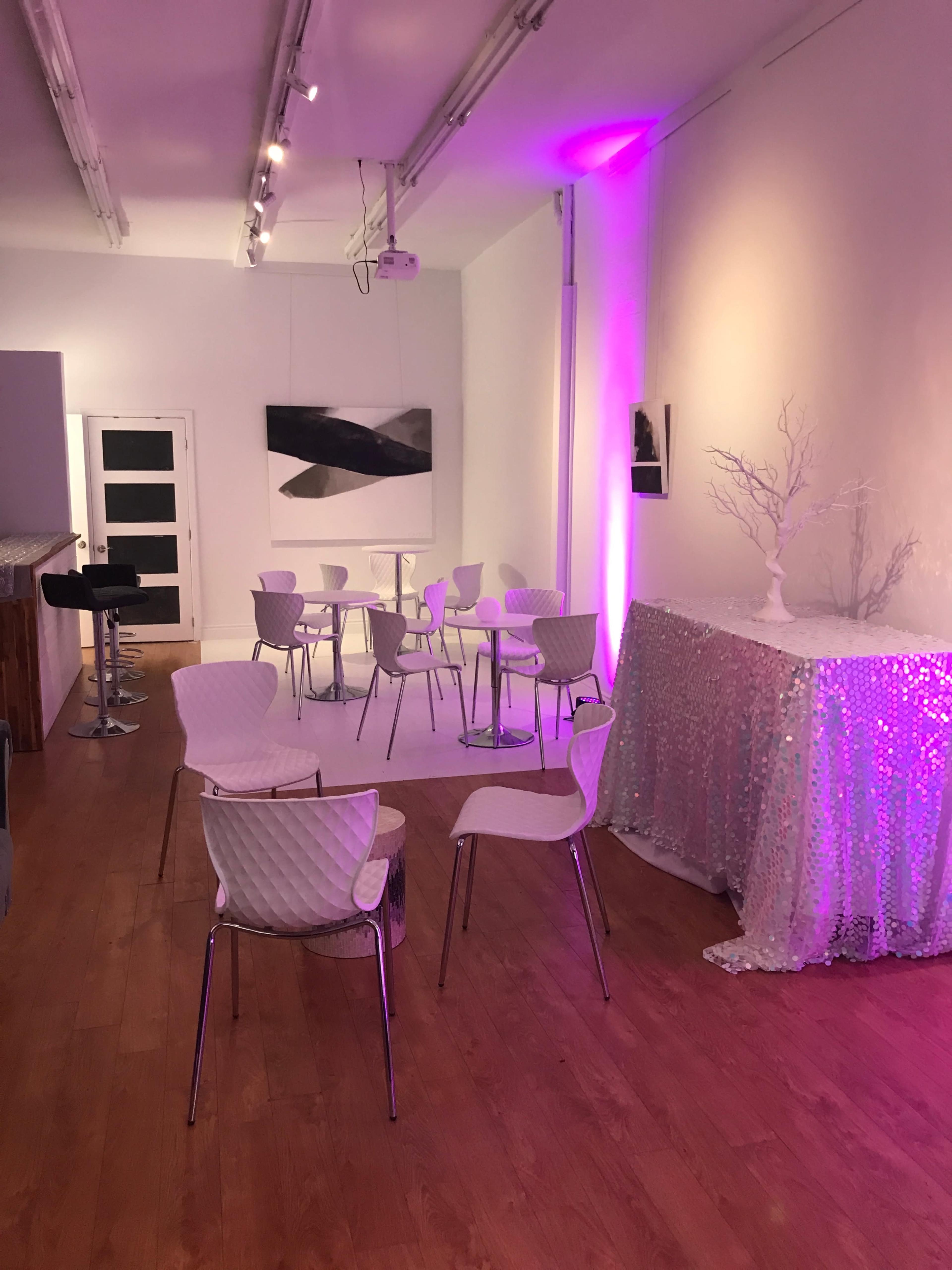 A modern, minimalist interior with several white chairs and tables, illuminated by soft purple lighting.