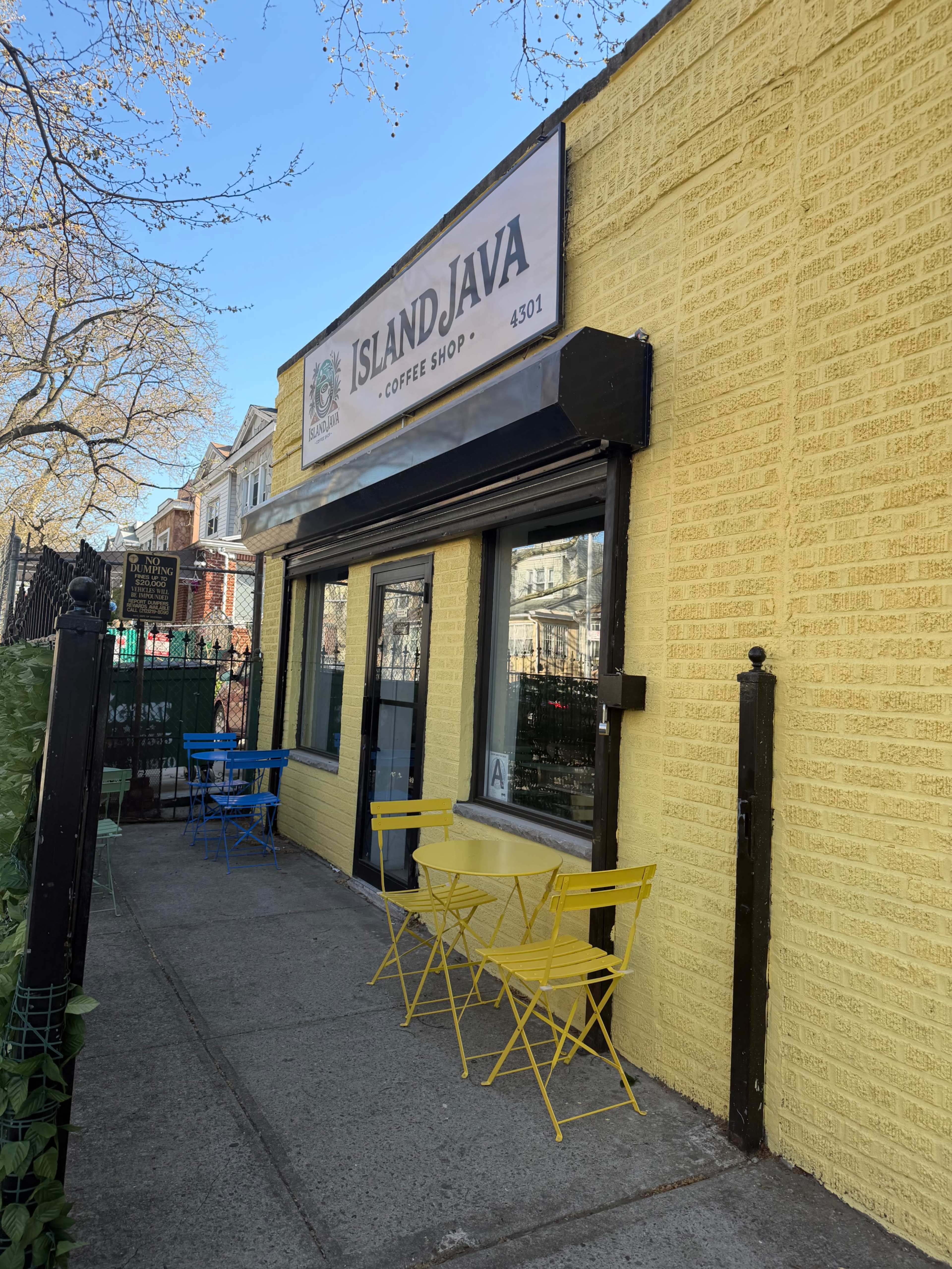 The image shows a yellow-painted coffee shop called "Island Java," featuring blue and yellow bistro tables outside on the sidewalk.