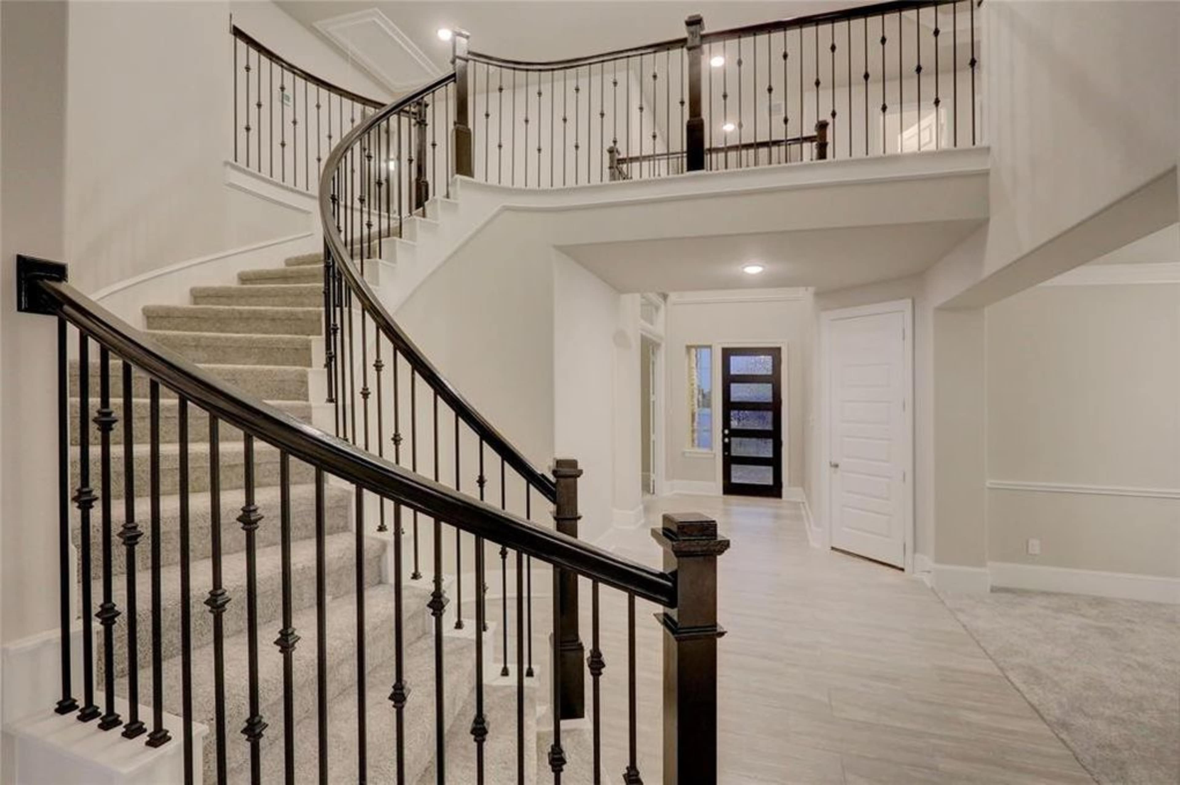 A spiral staircase with black wrought iron railings leads to a second level in a spacious foyer with light-colored walls and wood flooring.