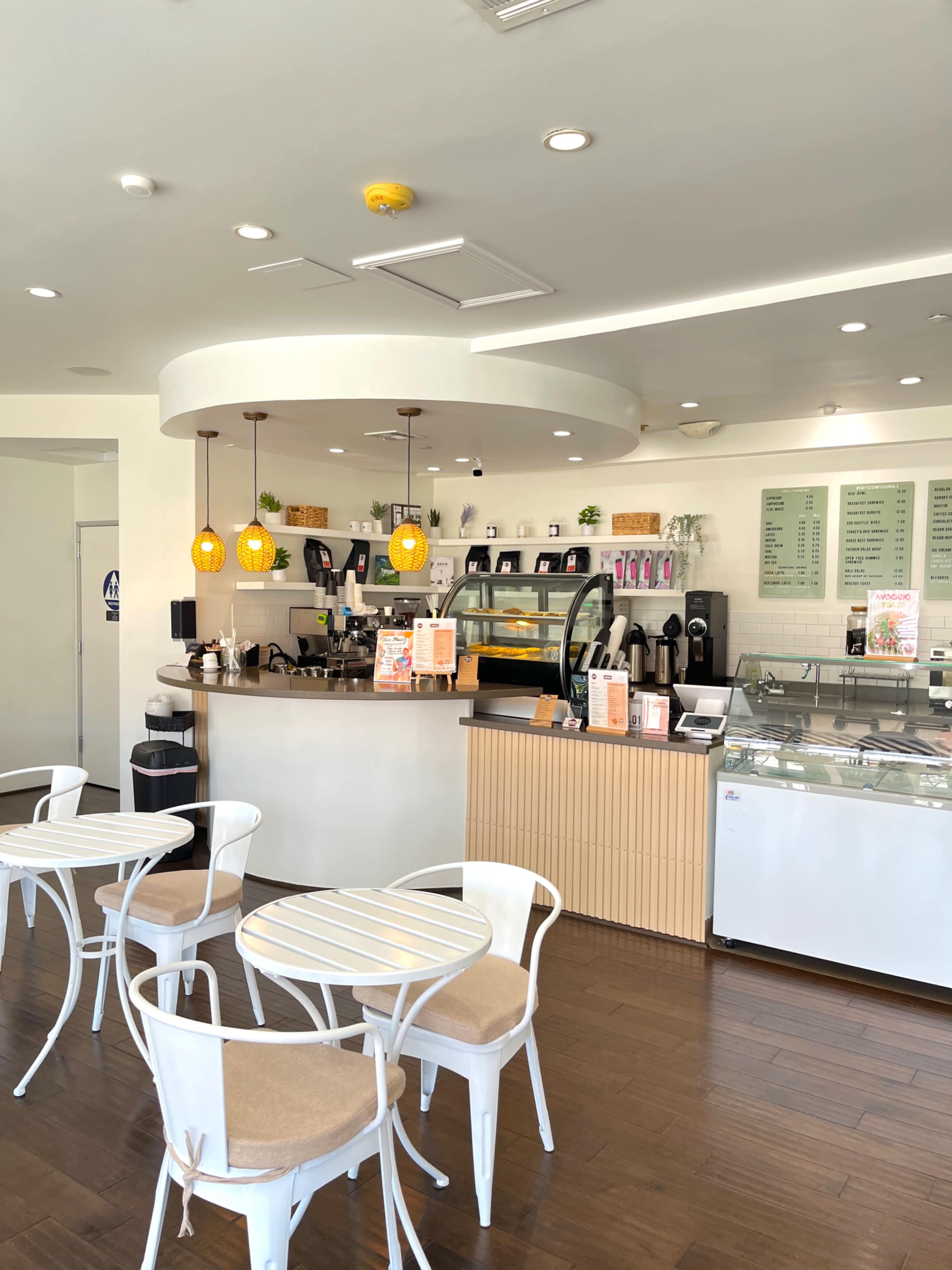 The image shows a bright, modern café with a display counter, seating area, and decorative lighting.