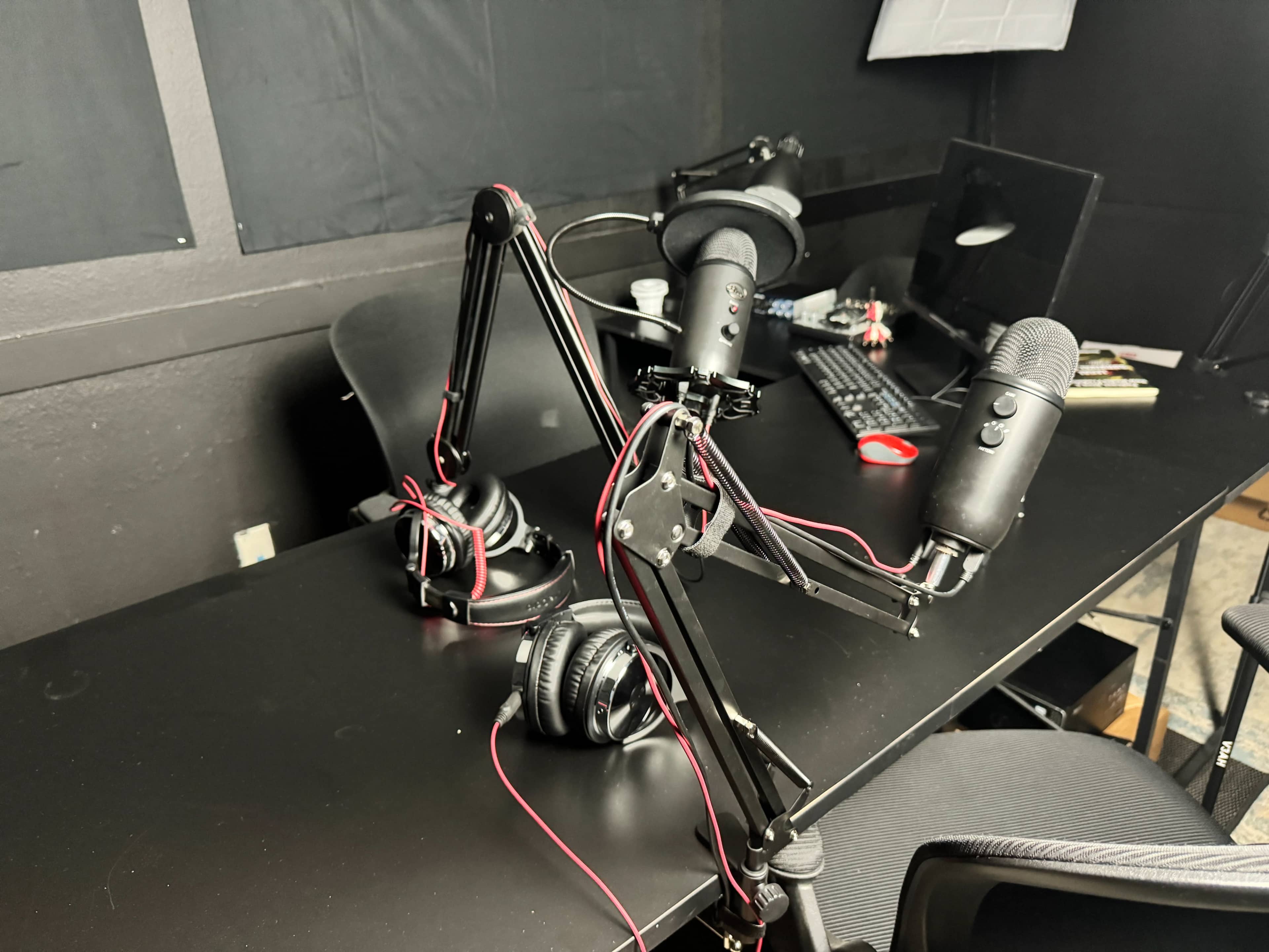 The image shows a black desk with a microphone setup, two headsets, and a computer keyboard.
