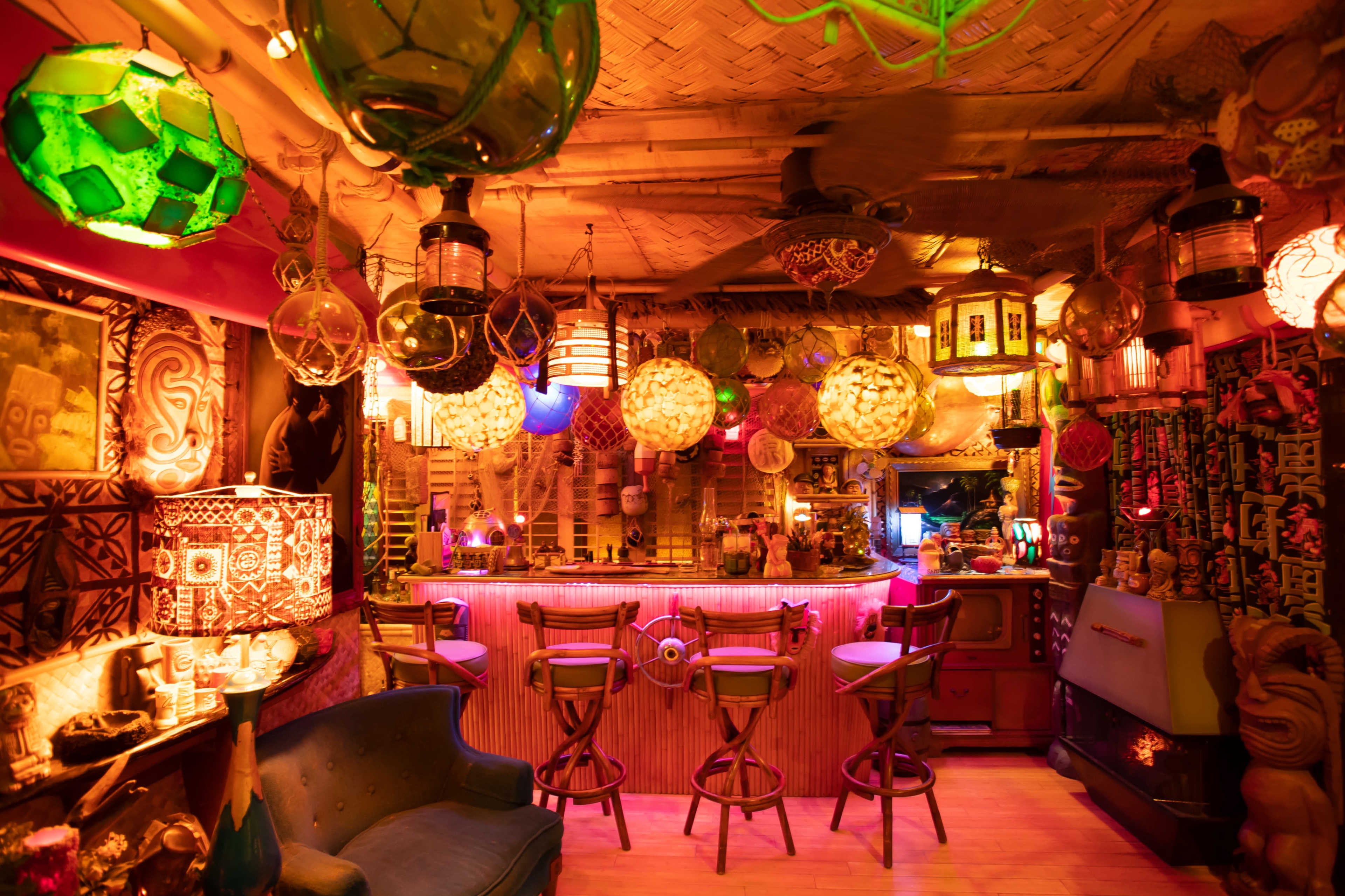 A vibrant tiki-themed bar with colorful lanterns, a circular bar counter, and various decorations on the walls.