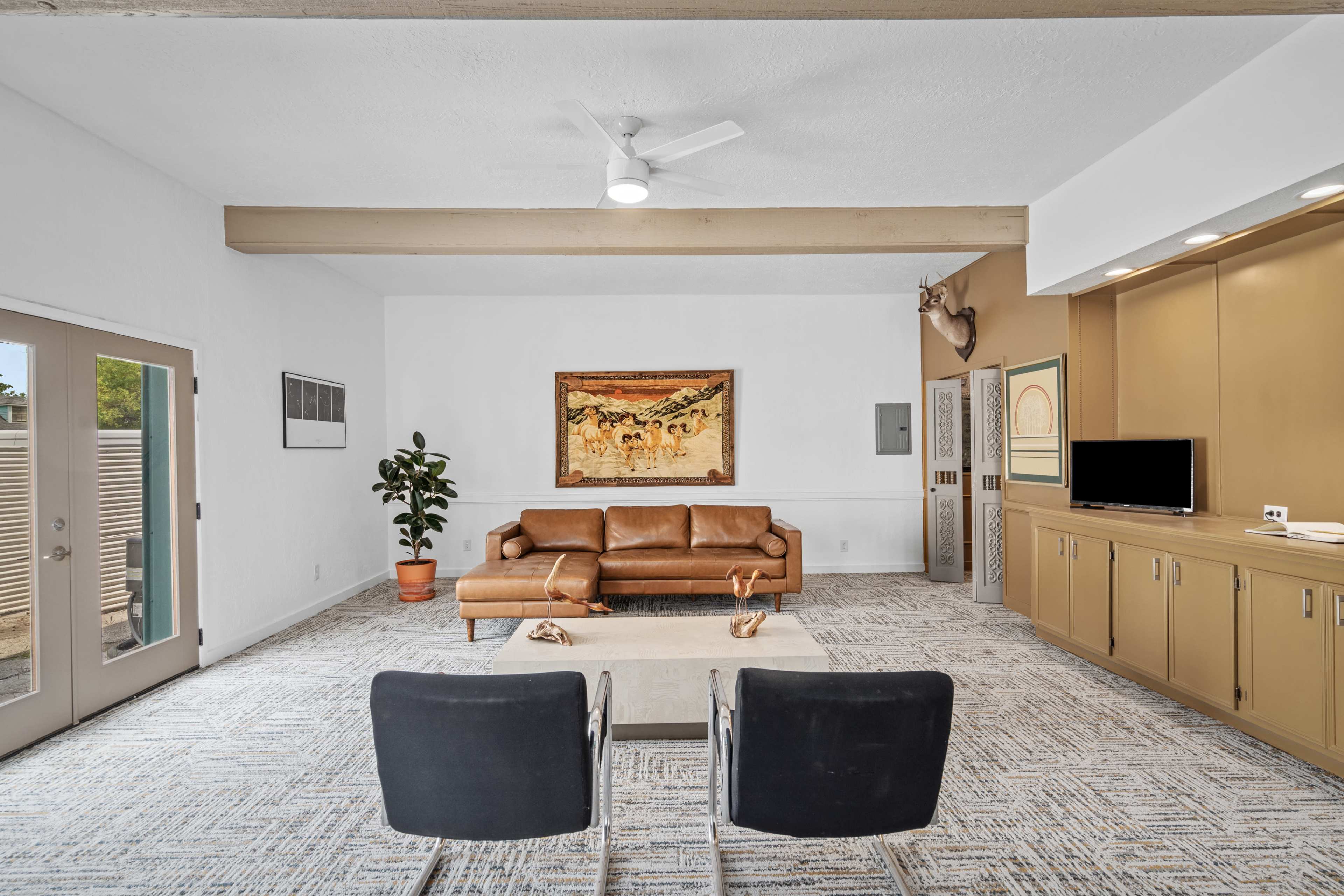 The image shows a spacious living area featuring a brown leather sofa, a coffee table, two black chairs, and a large artwork on the wall.