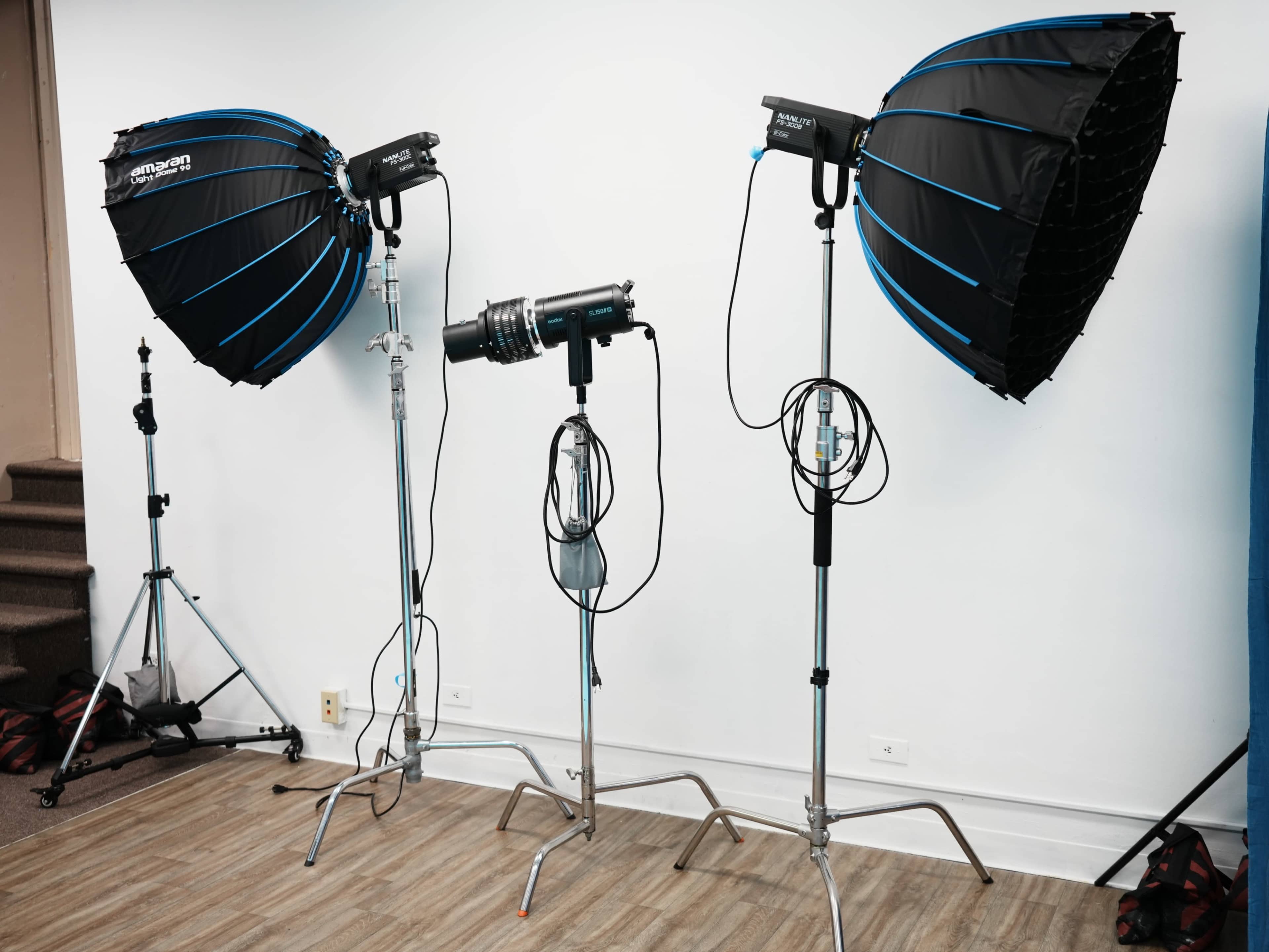 Two large photography light modifiers are positioned on stands, with a central light source and additional equipment in an indoor studio setting.
