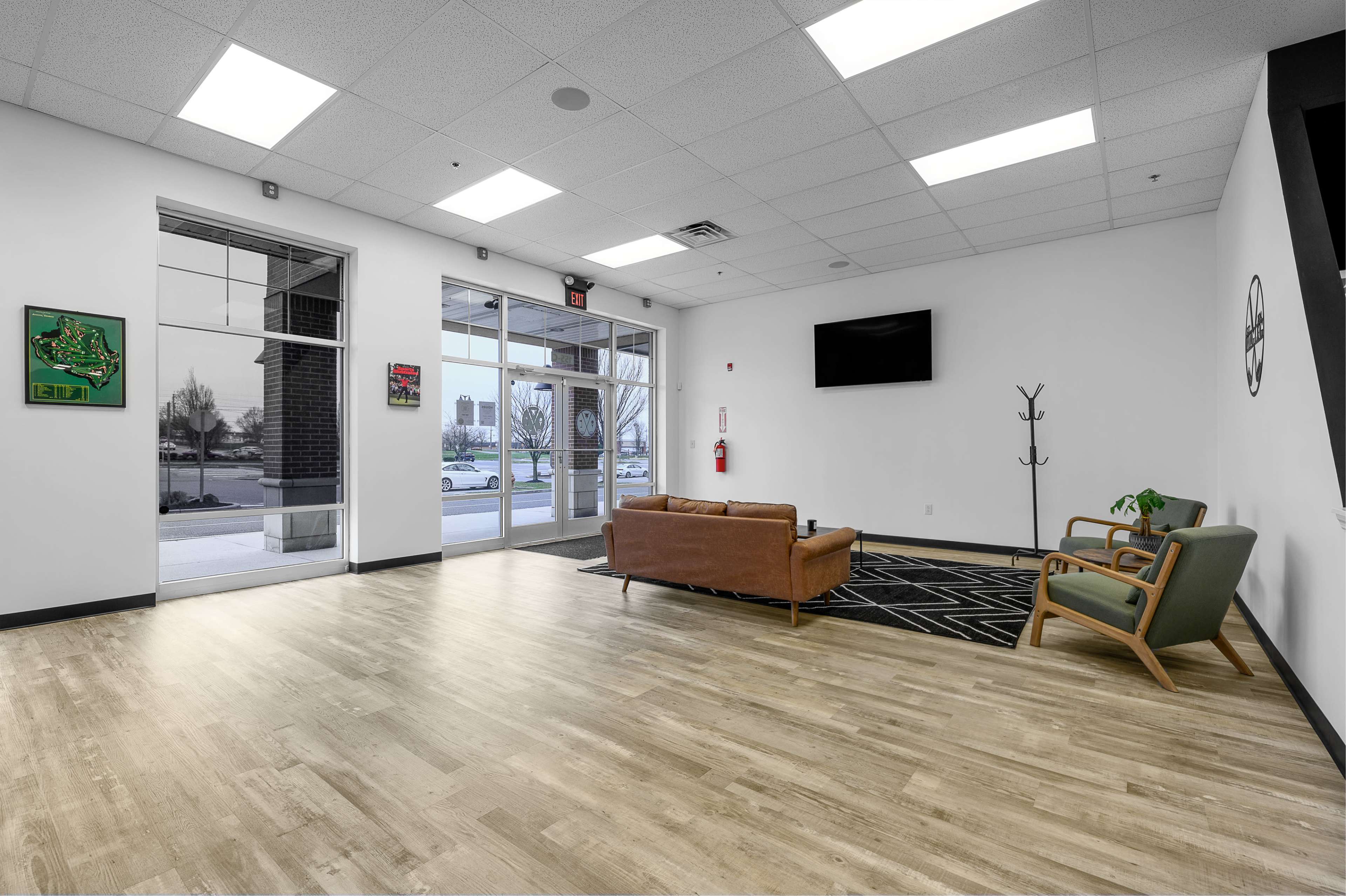 A spacious, modern lobby features a seating area with a couch and chairs, large windows, and a television mounted on the wall.