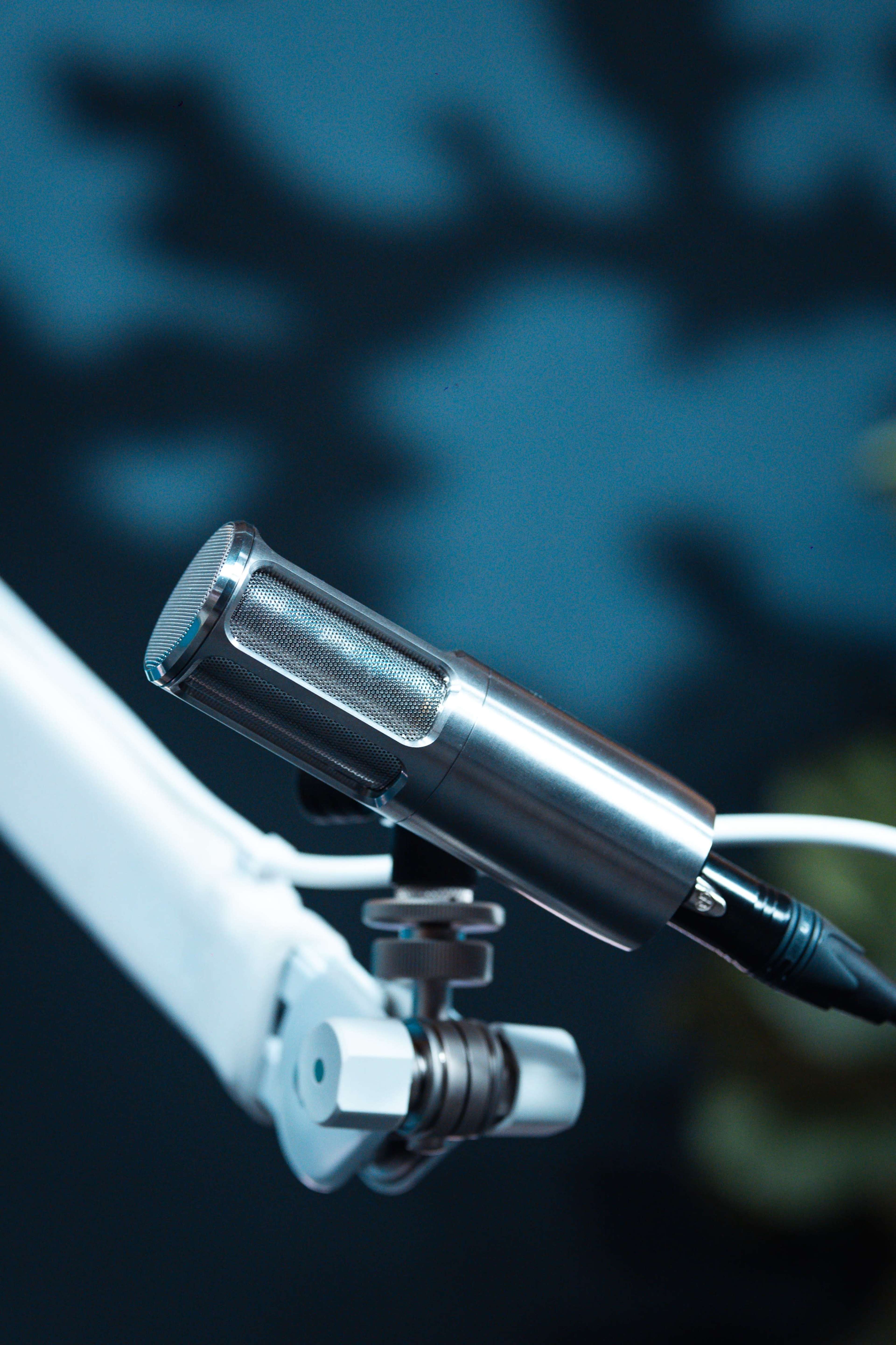 A close-up of a metallic microphone attached to a white adjustable arm on a blurred blue background.