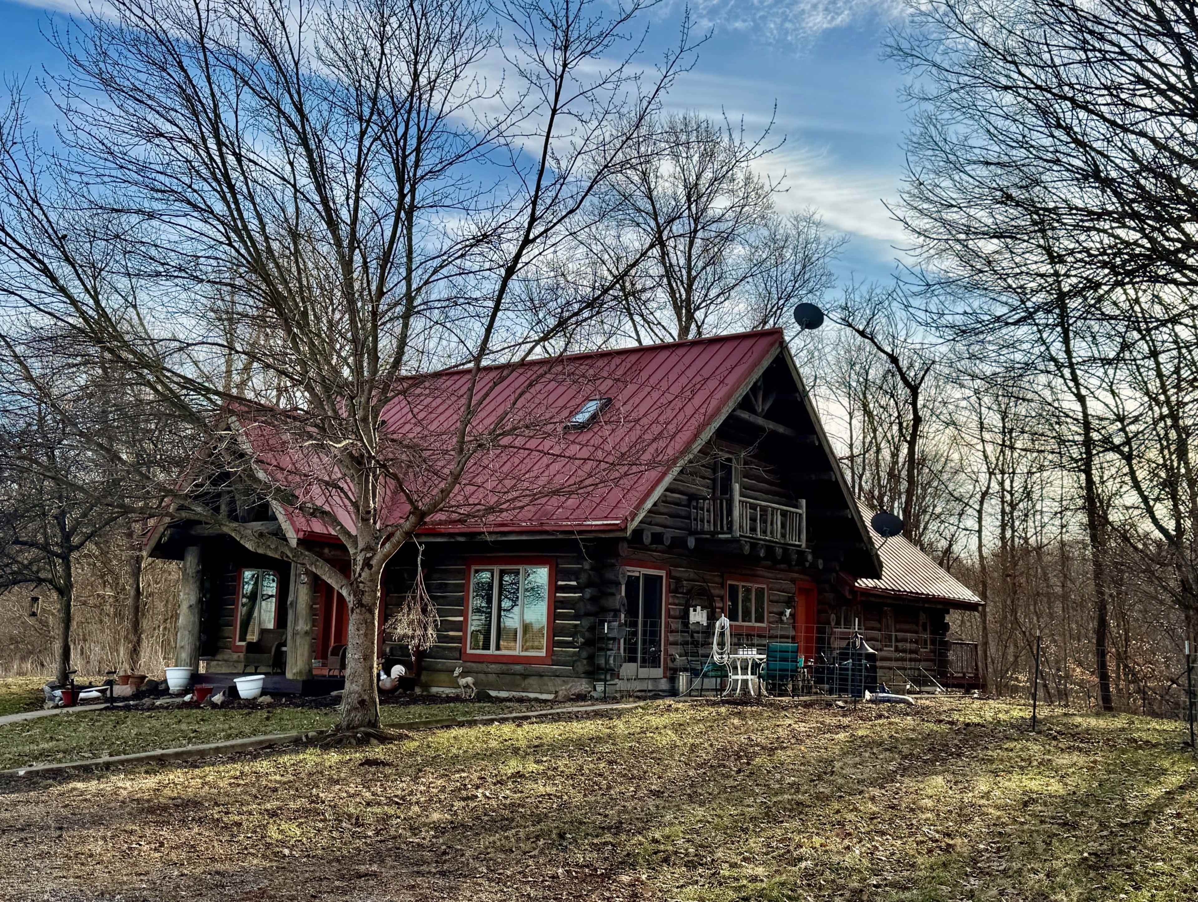 A log cabin with a red metal roof is surrounded by bare trees and a grassy area.