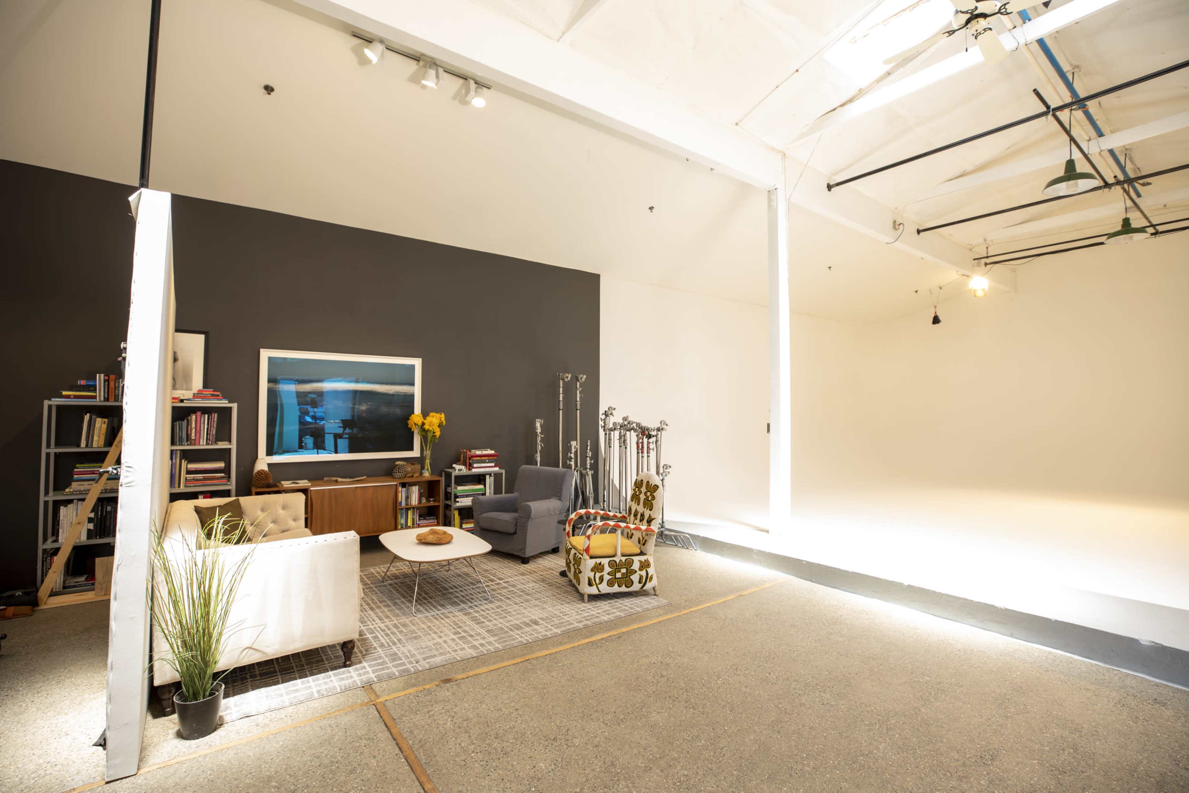 A spacious studio featuring a gray accent wall, a white sofa, a wooden coffee table, and a gray armchair, along with bookshelves and decorative items.