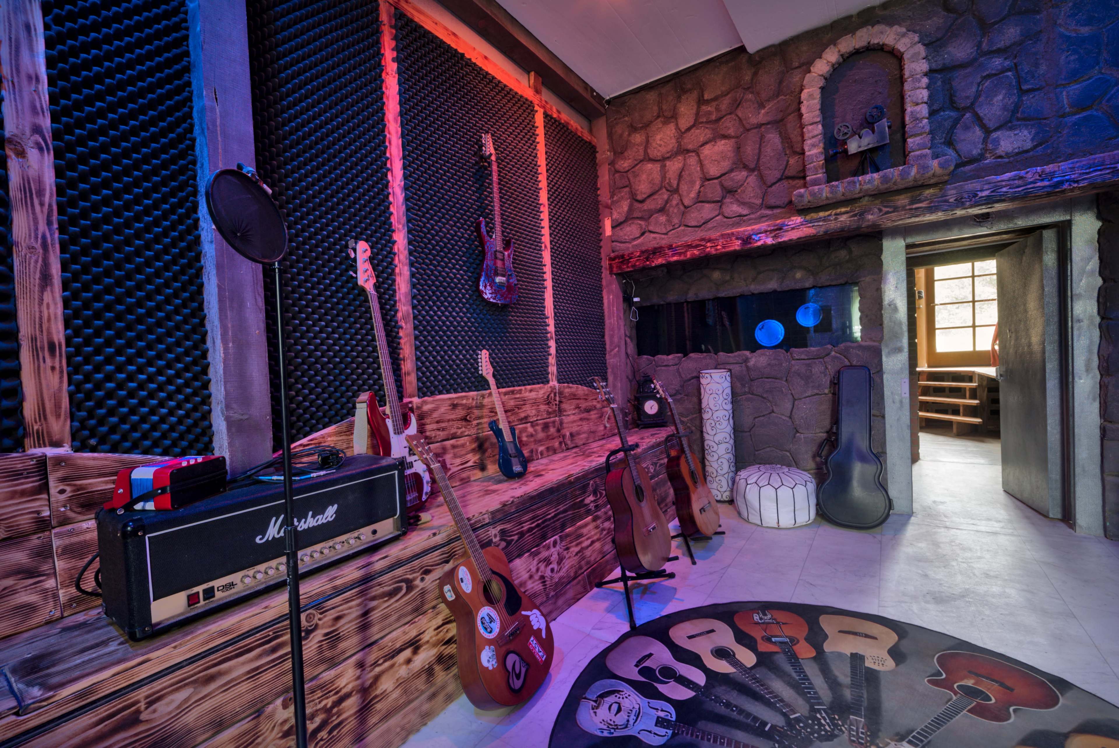 The image shows a music room with various guitars displayed on the walls and a Marshall amplifier positioned near a wooden bench.