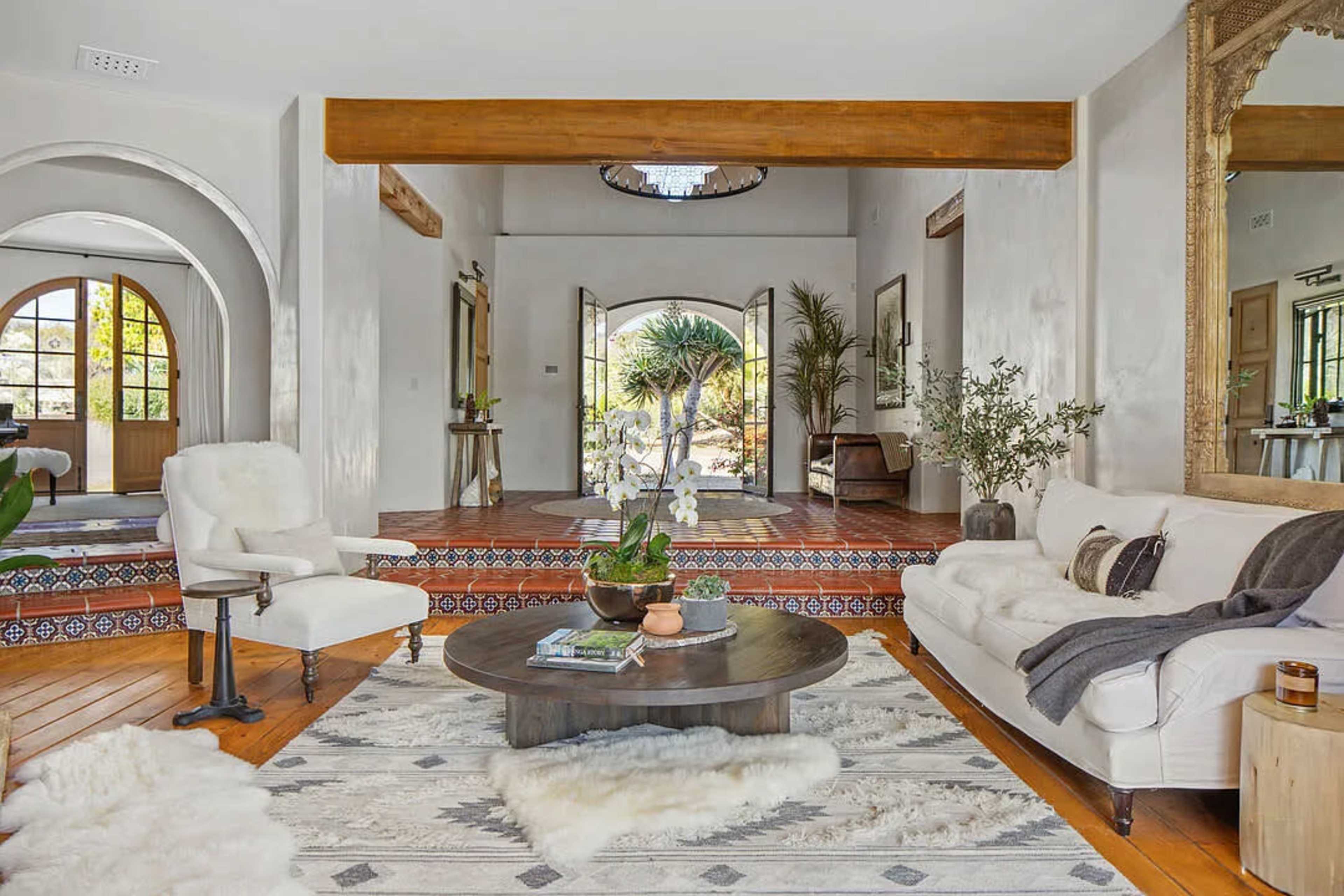 The image shows a spacious living room with a white sofa, a round coffee table, and a view of an outdoor area through large arched doors.