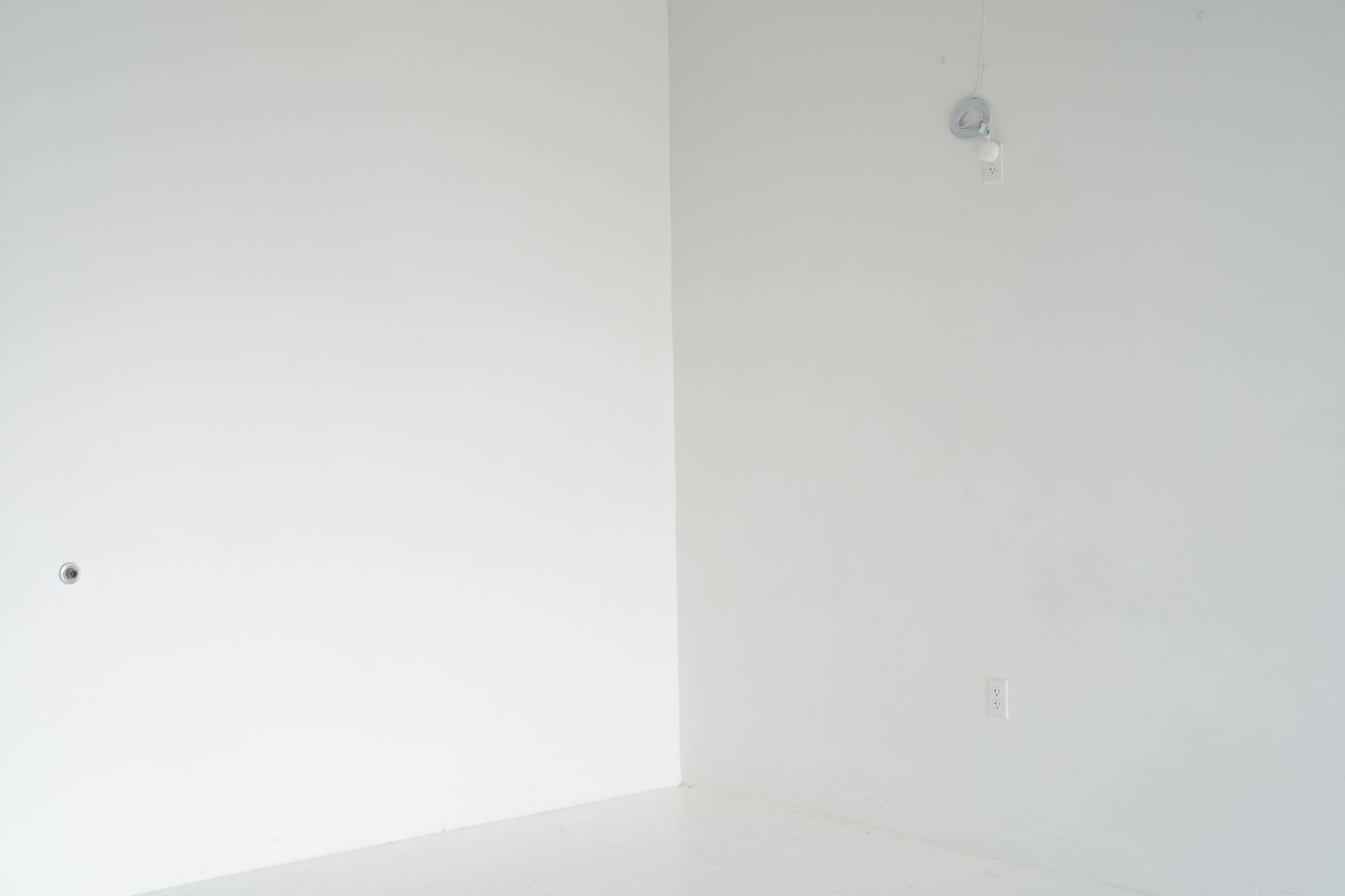 A mostly empty room with white walls and a single light fixture hanging from the ceiling.