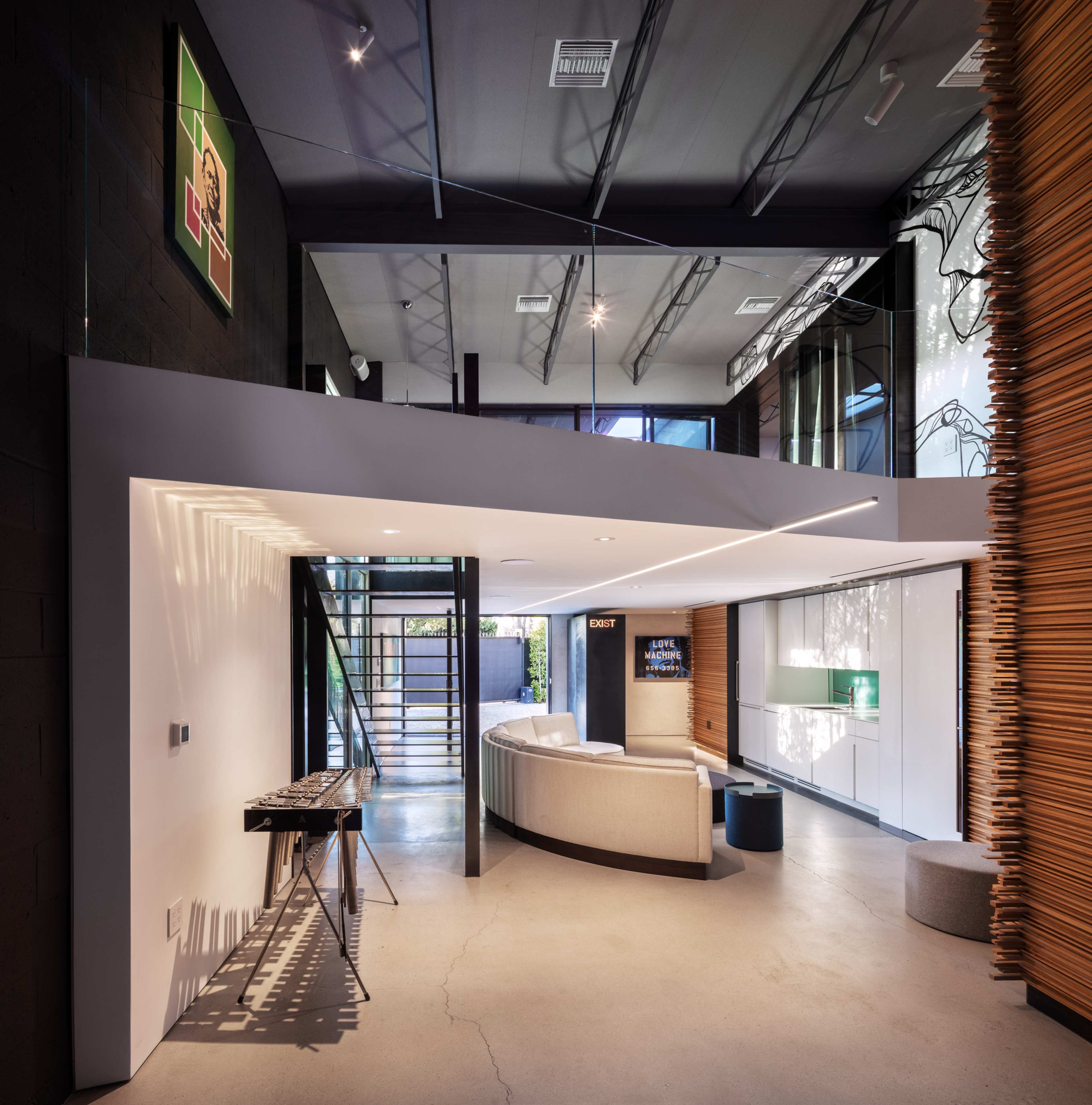 The image shows a modern interior space featuring an open layout with a curved sofa, a staircase, and artwork on the walls.