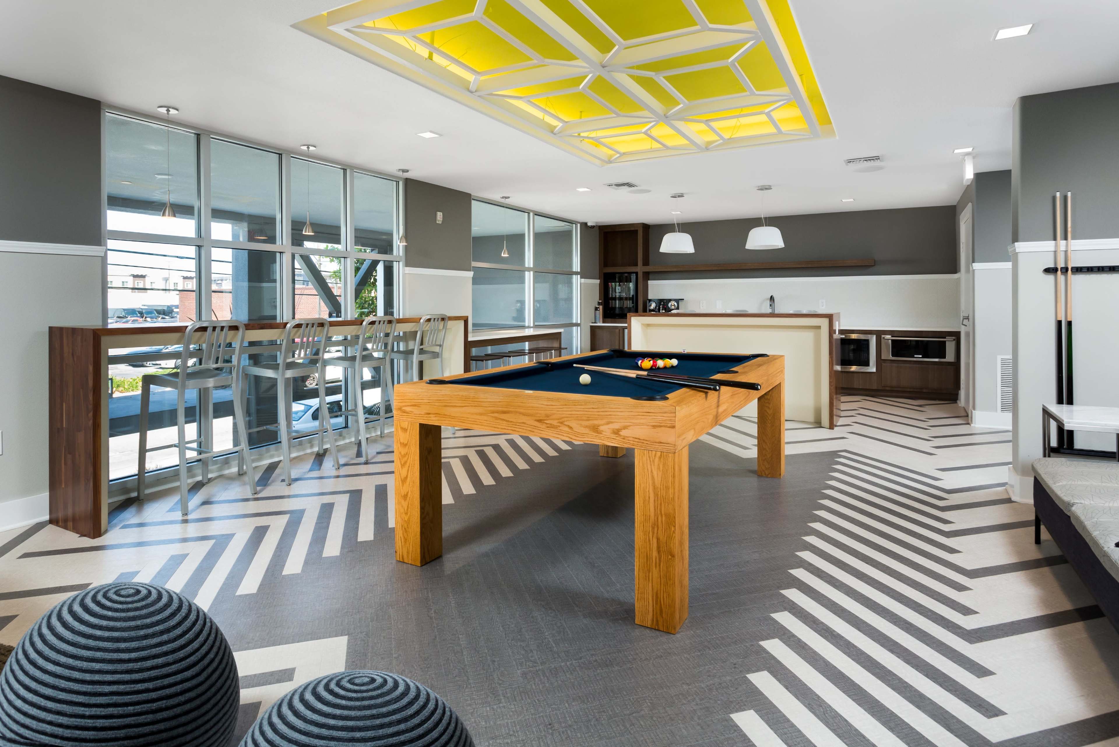 A modern game room with a pool table, bar seating, and stylish geometric flooring.
