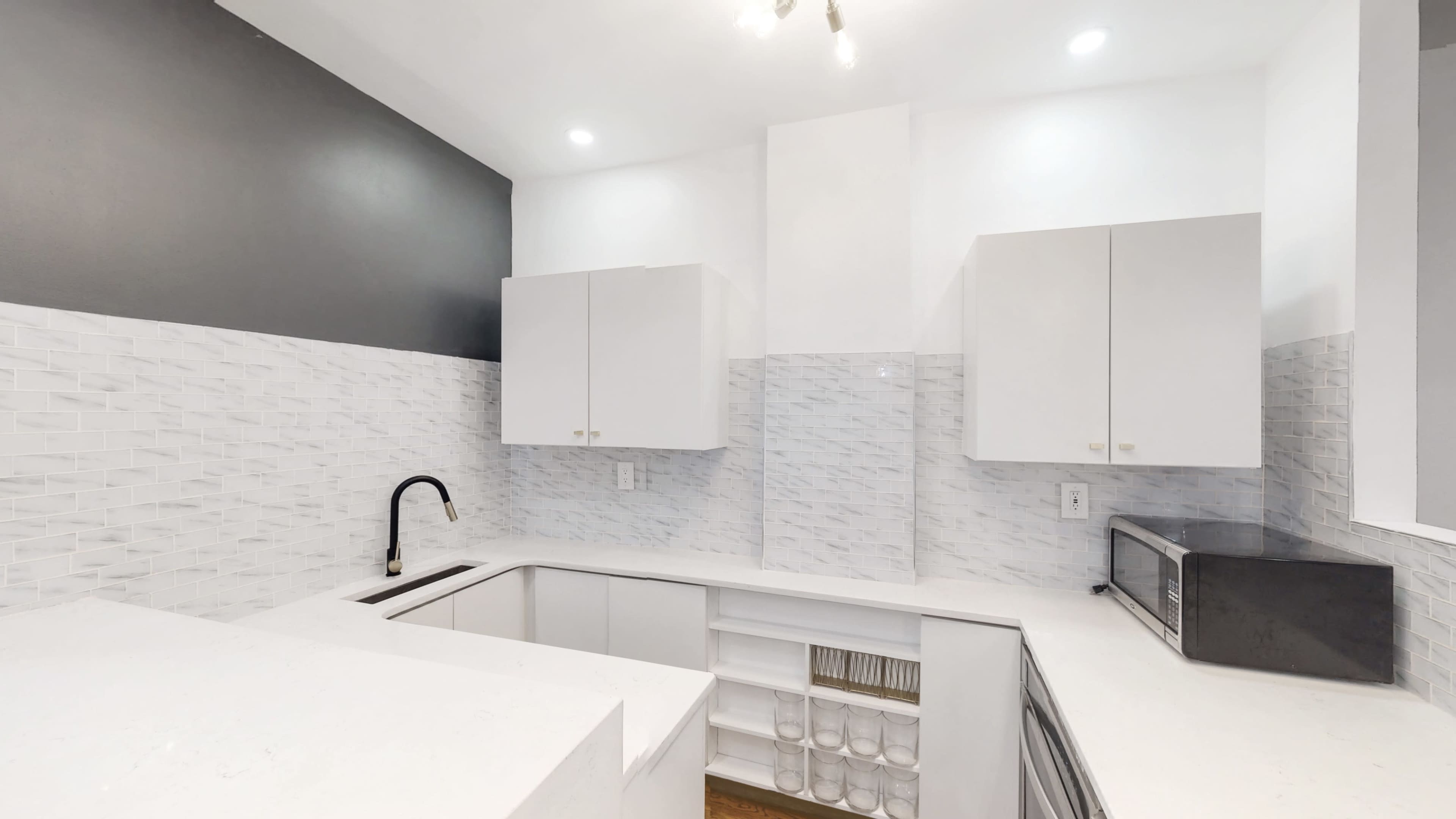 A modern kitchen features white cabinetry with a contrasting dark wall and a minimalist design.