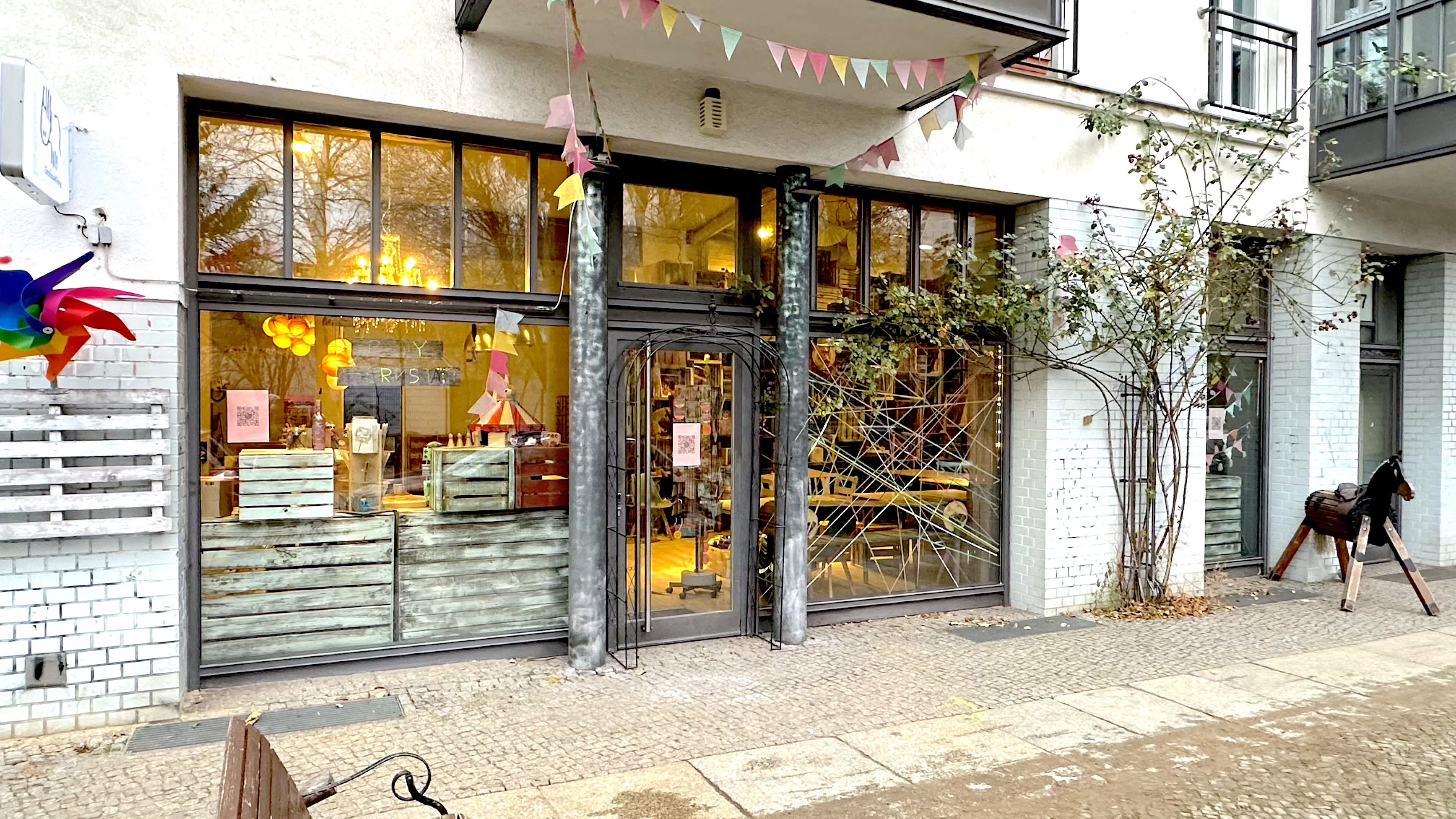 The image shows the exterior of a storefront with large glass windows, wooden decor, and colorful bunting flags above the entrance.