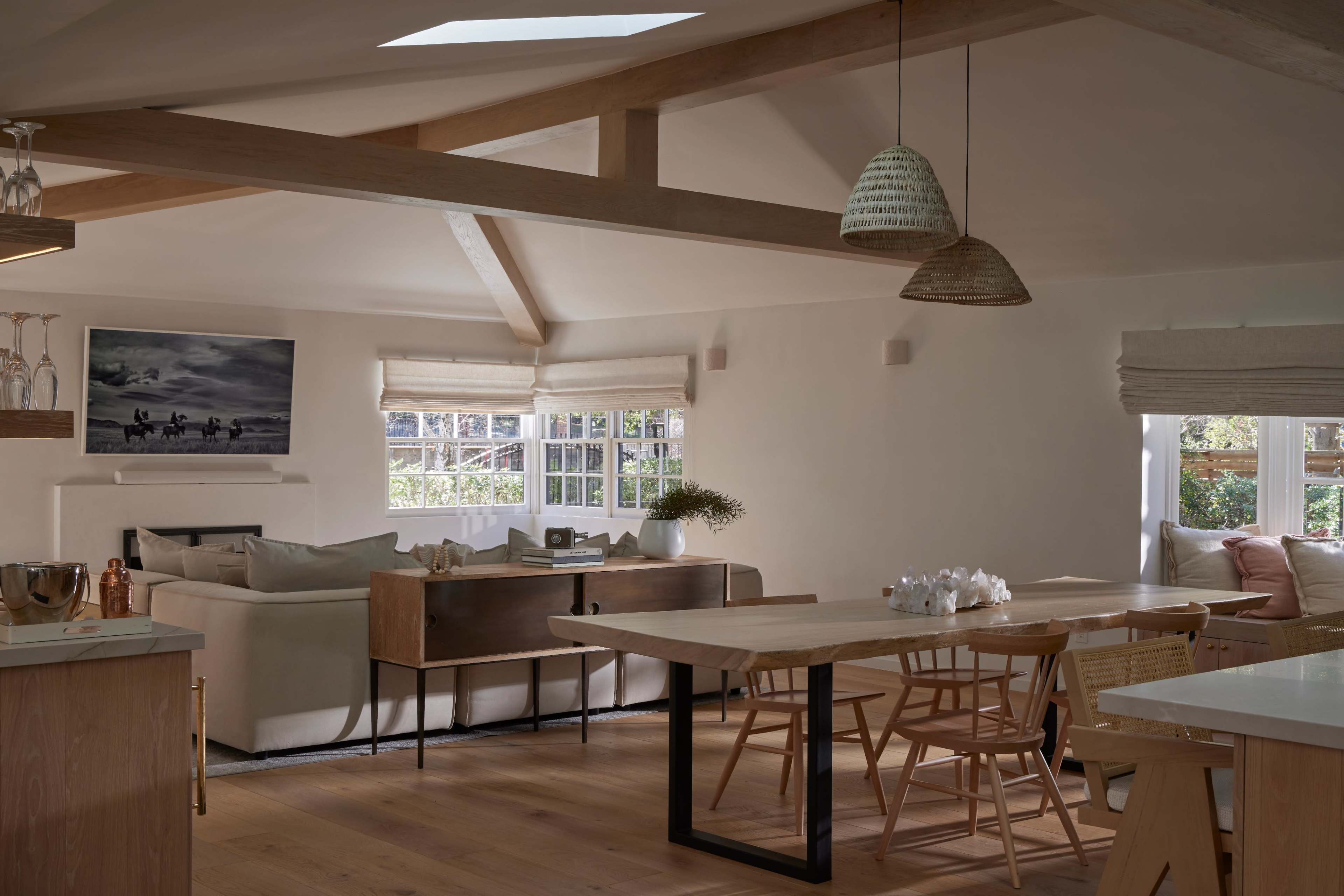 The image shows a modern, open-concept living space with a dining area, a comfortable sofa, and large windows allowing for natural light.