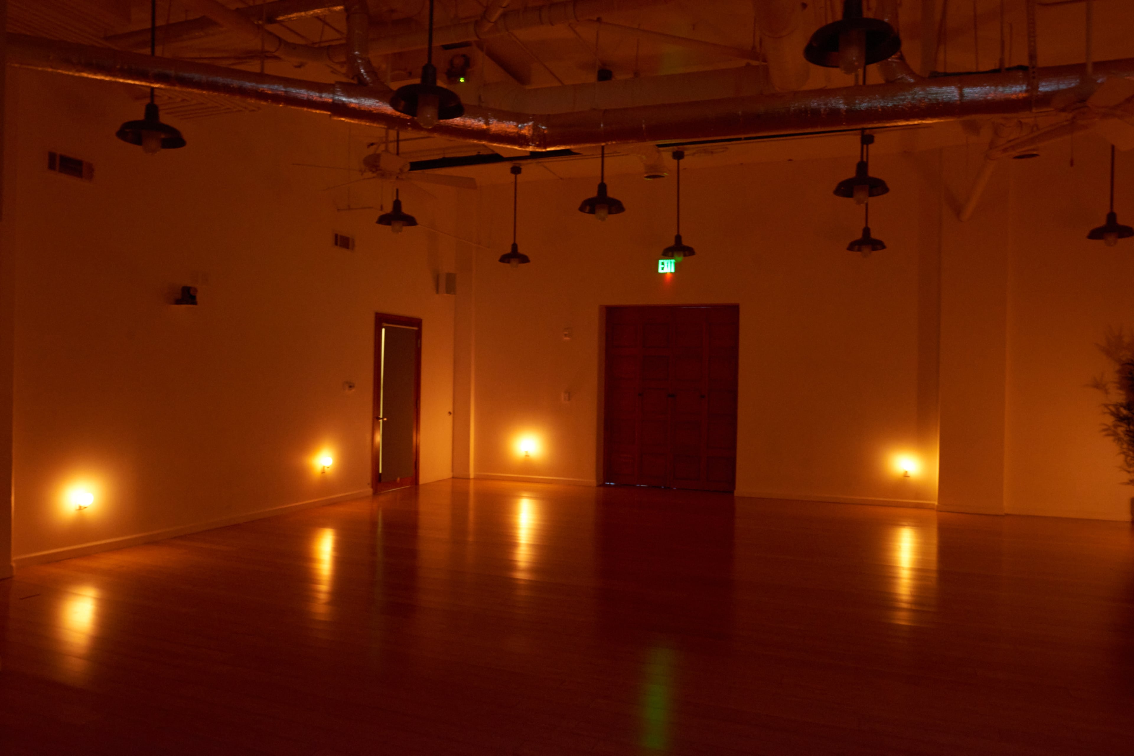 A dimly lit interior space with hardwood floors, featuring minimalist lighting fixtures and a large wooden door at one end.