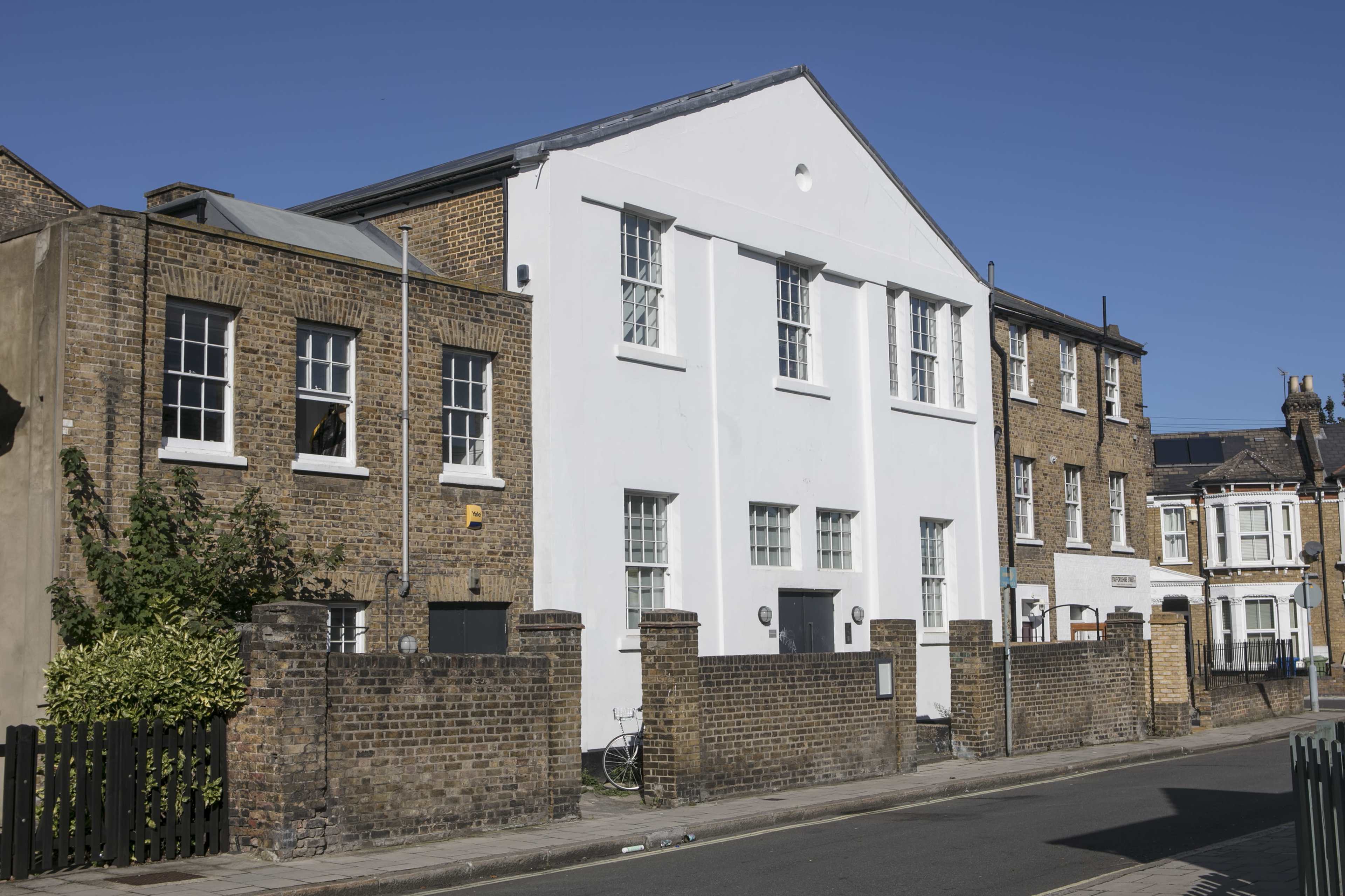 A row of buildings in a street, featuring a white structure with large windows alongside brick buildings.