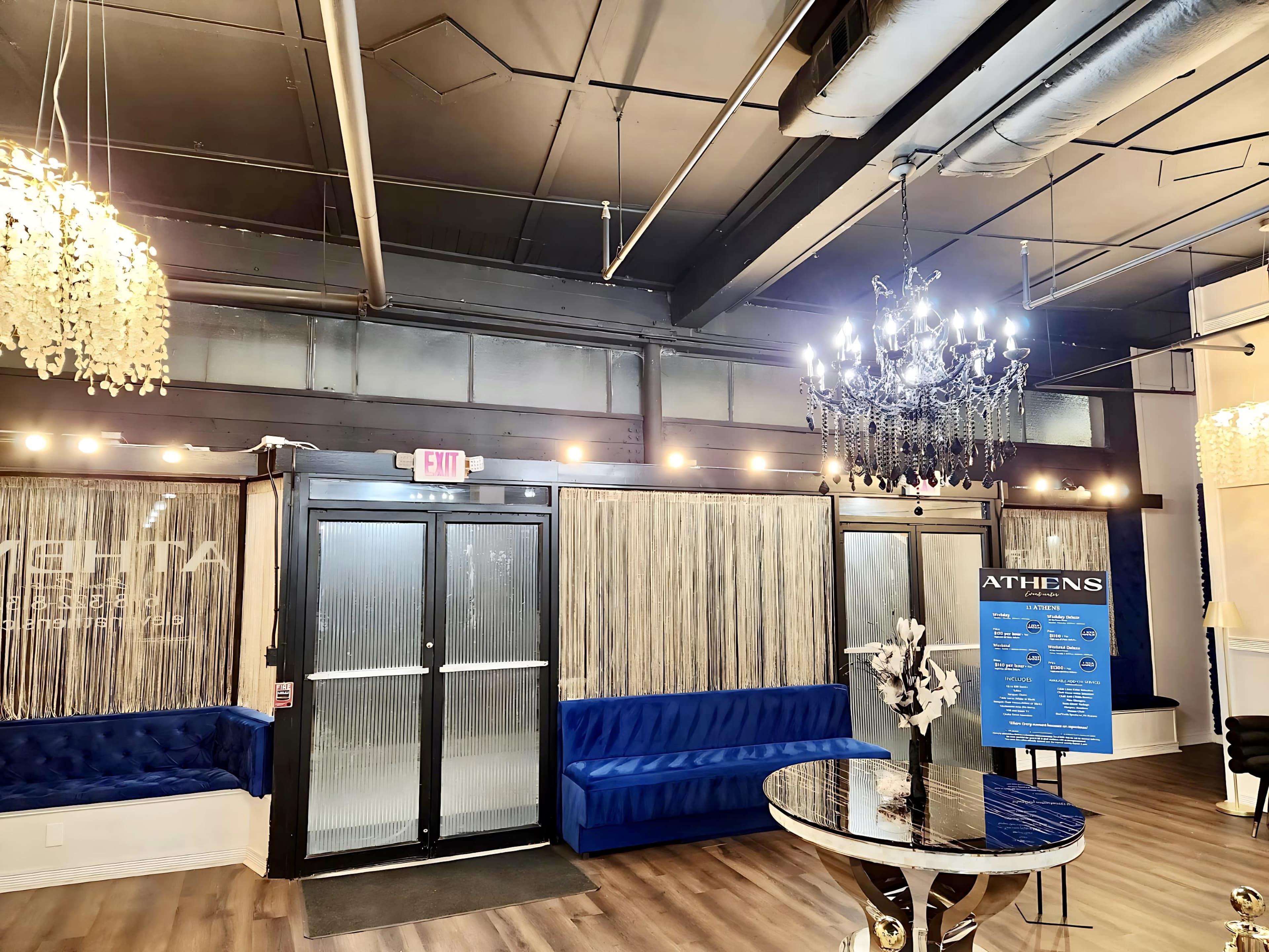 The image shows the interior of a modern venue featuring a blue upholstered bench, a chandelier, and a decorative sign.