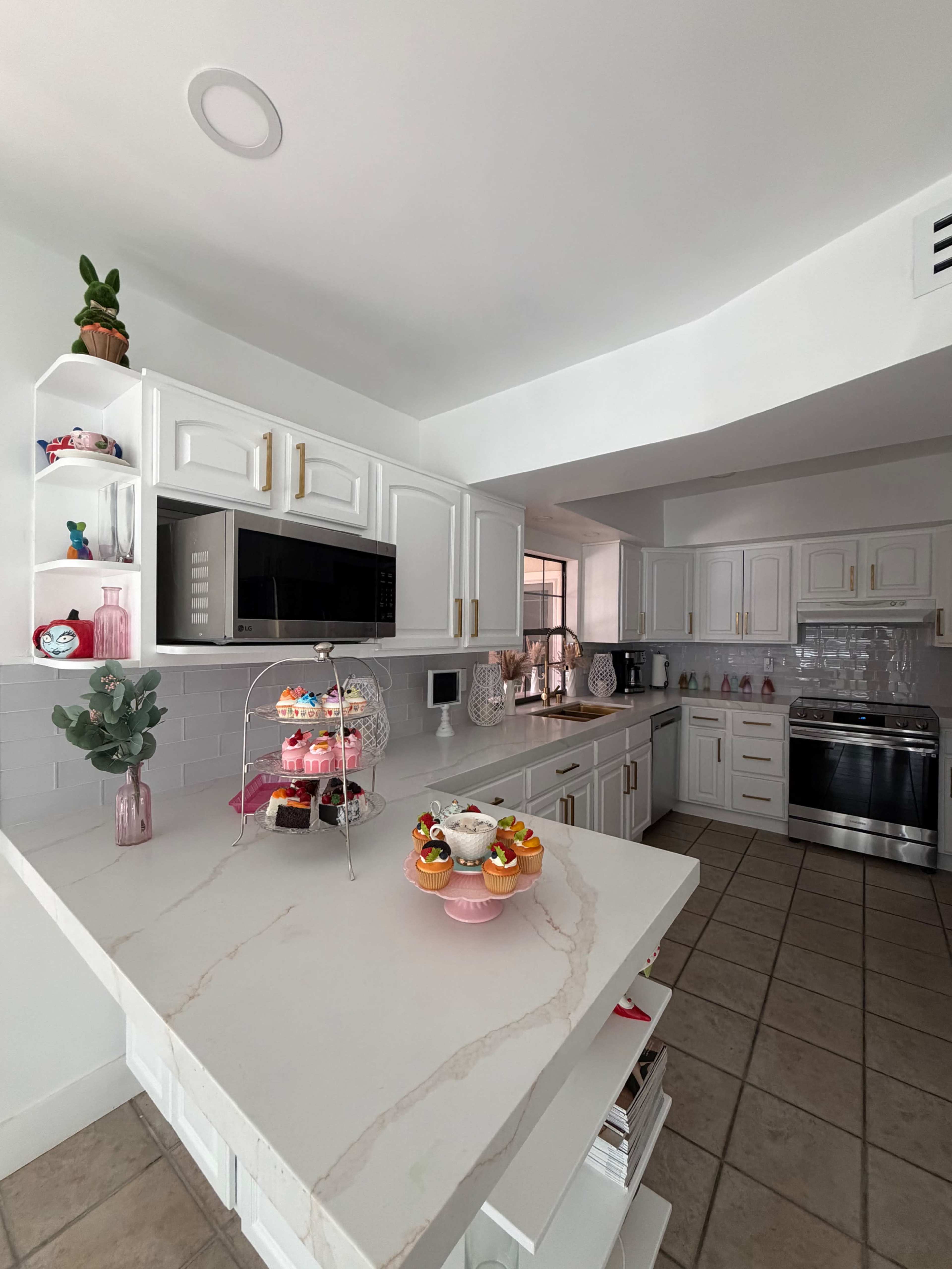 A modern kitchen features white cabinets, a marble-topped island, and various decorative items, including a multi-tiered display of colorful cupcakes.