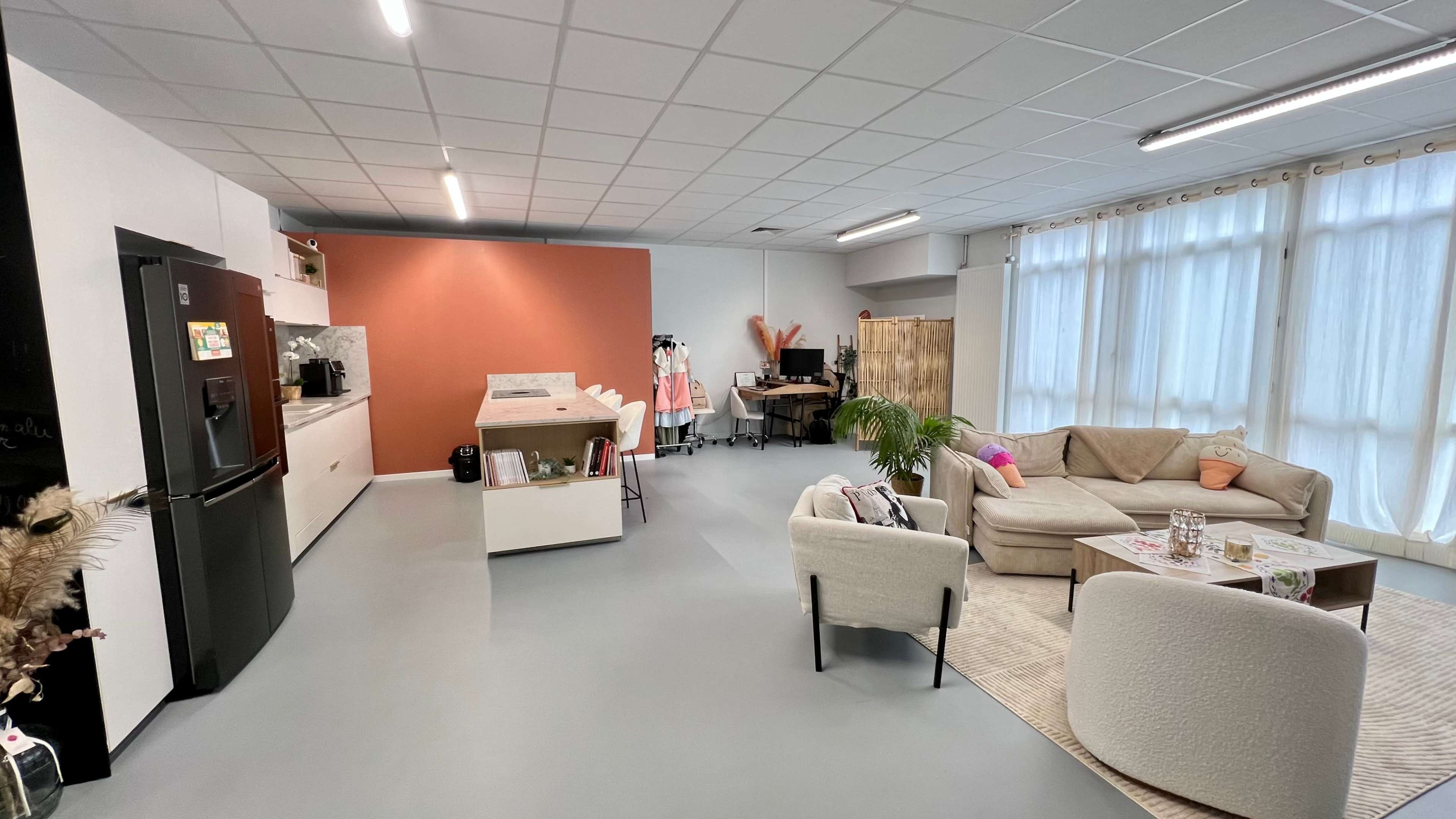 The image shows a modern open-plan office space with a kitchen area, seating, and workstations.