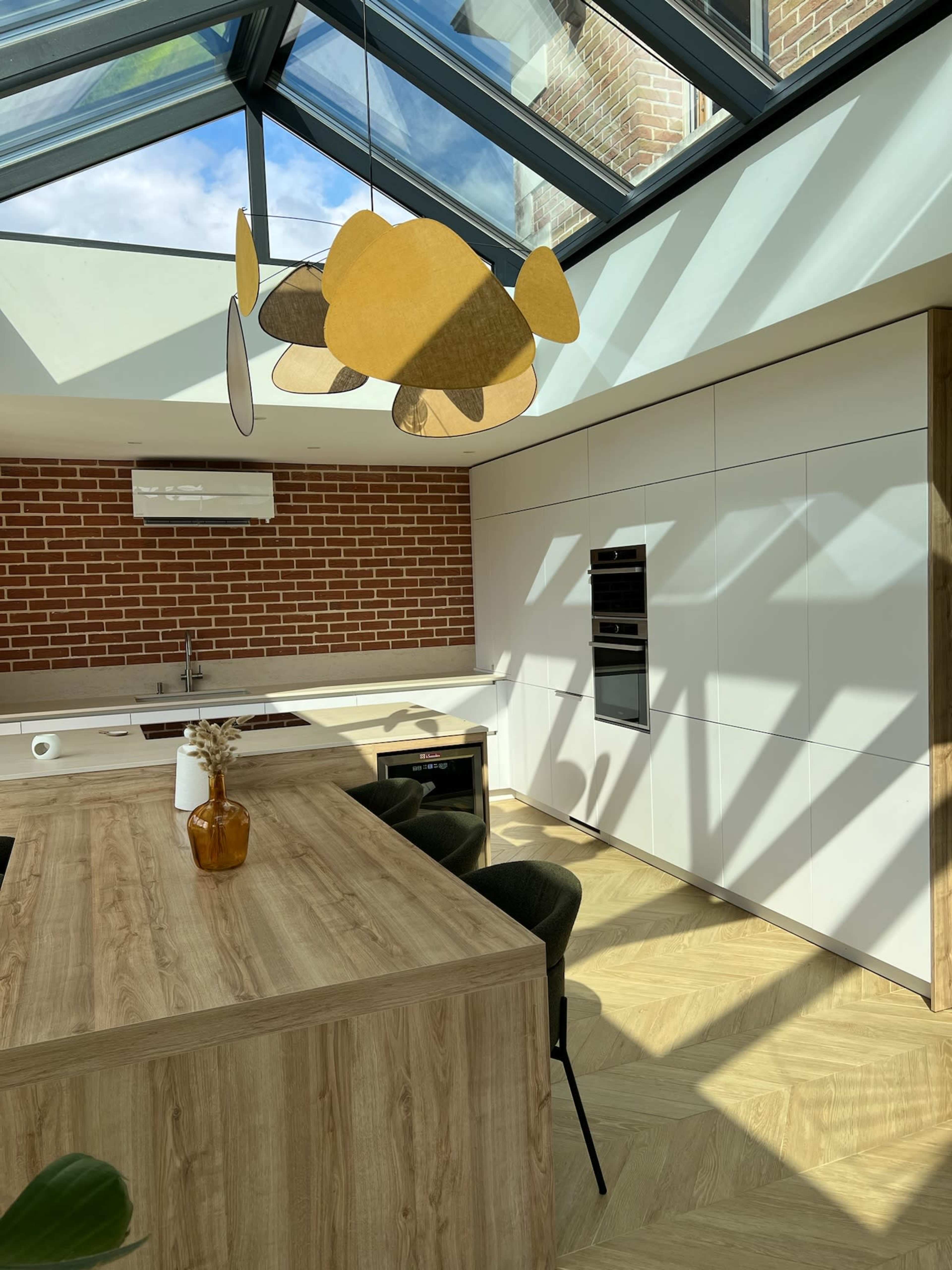 A modern kitchen with a wooden island, a geometric pendant light, and a skylight illuminating the space.