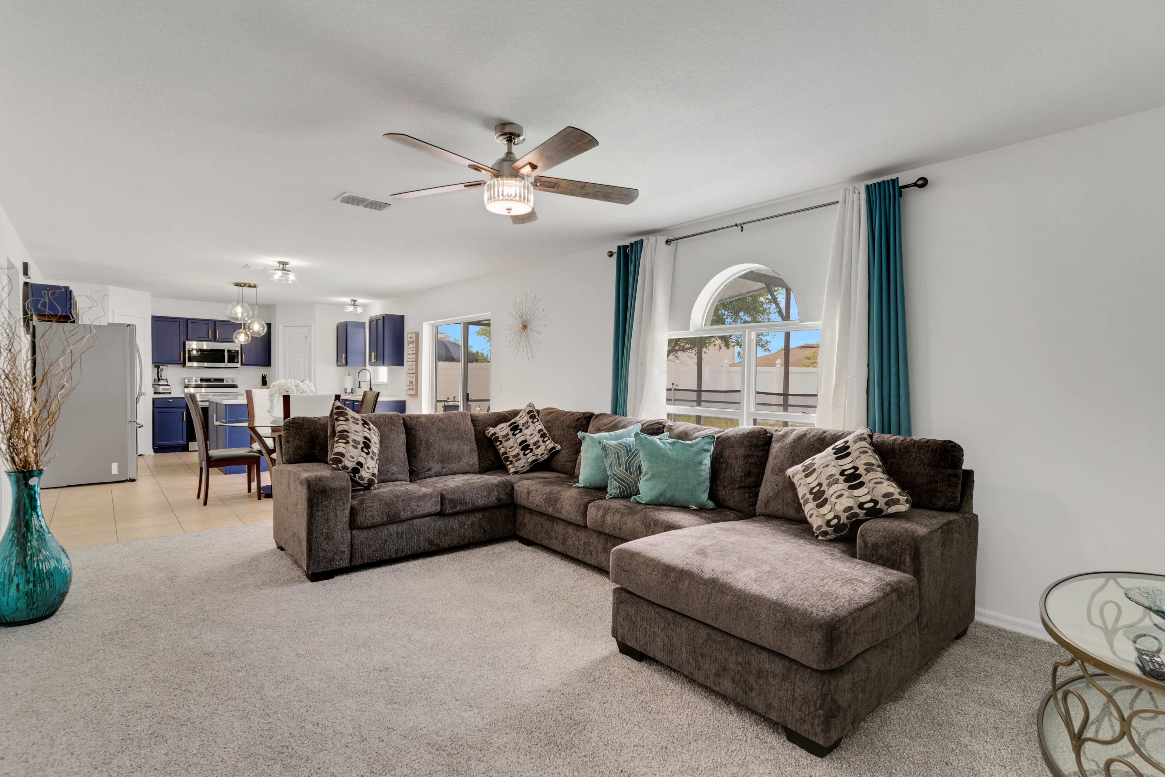 A living room with a large sectional sofa, a coffee table, and a kitchen area visible in the background.