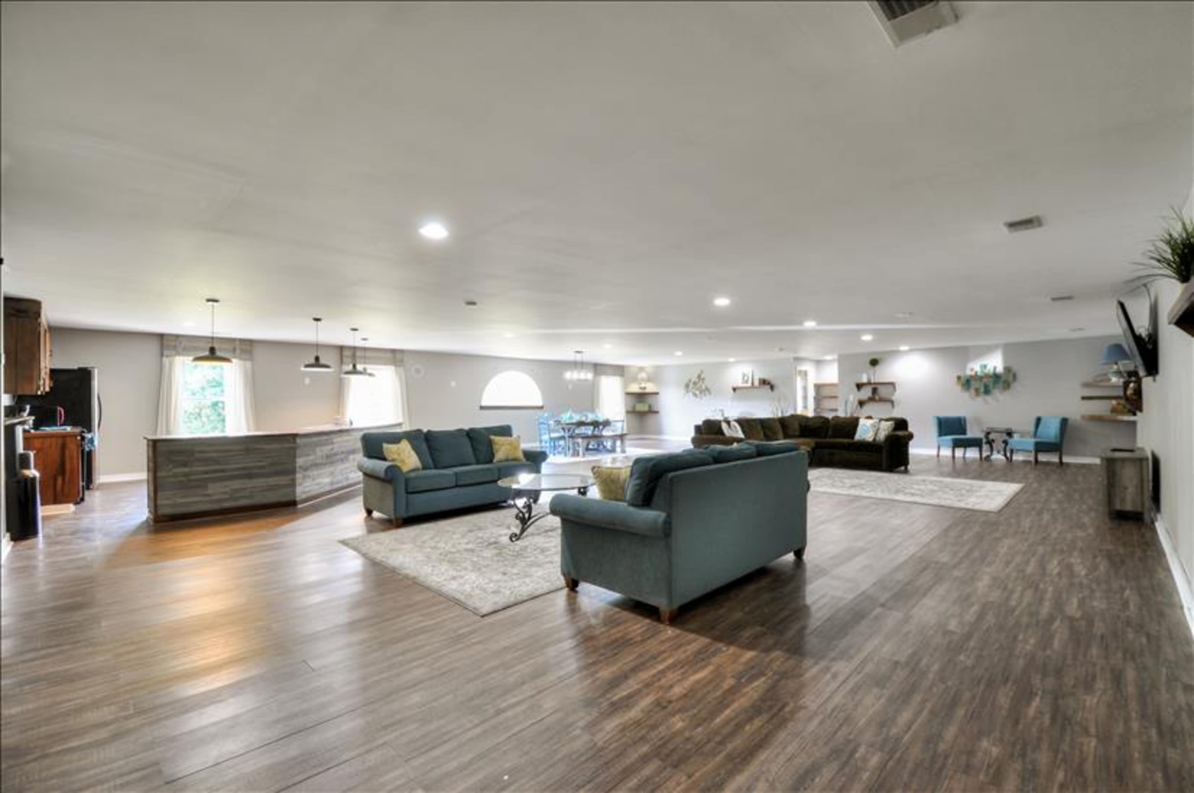 A spacious living area with two sets of sofas, a small dining table, and a kitchen bar in an open layout.