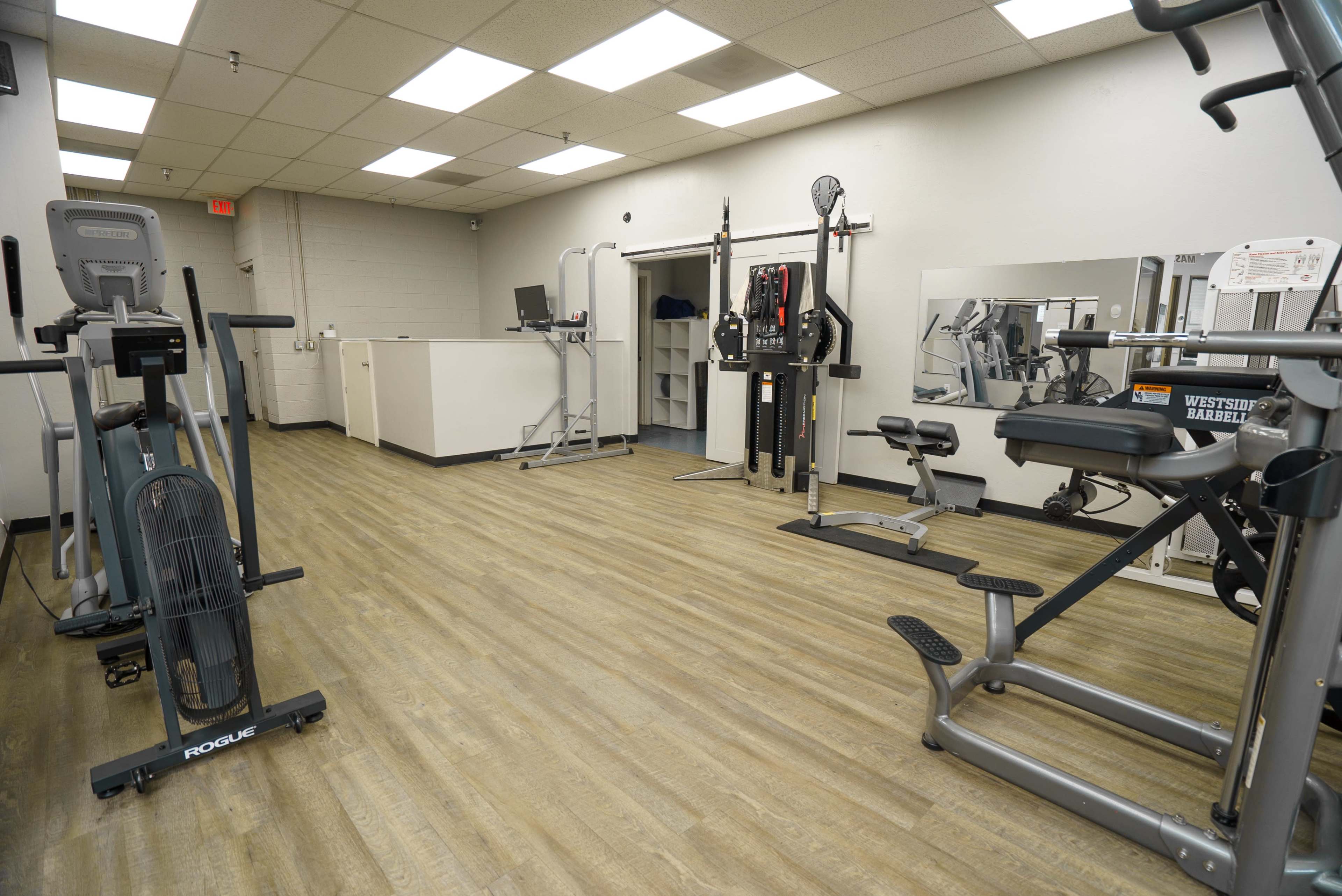The image shows an empty gym interior with various exercise equipment, including treadmills and weight machines, arranged along the walls and flooring.