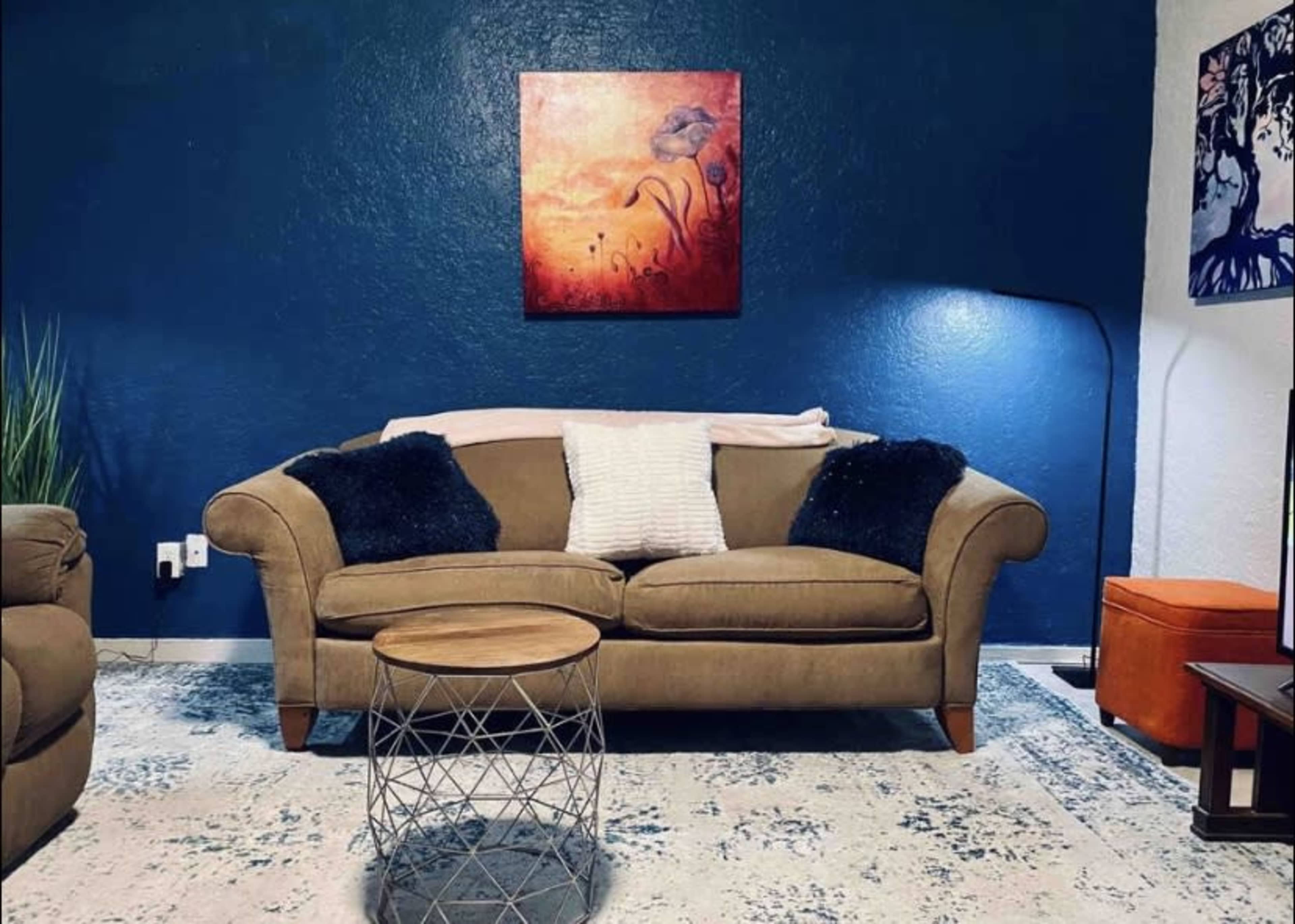A beige sofa with throw pillows sits against a blue wall, accompanied by a small round coffee table and a floor lamp.