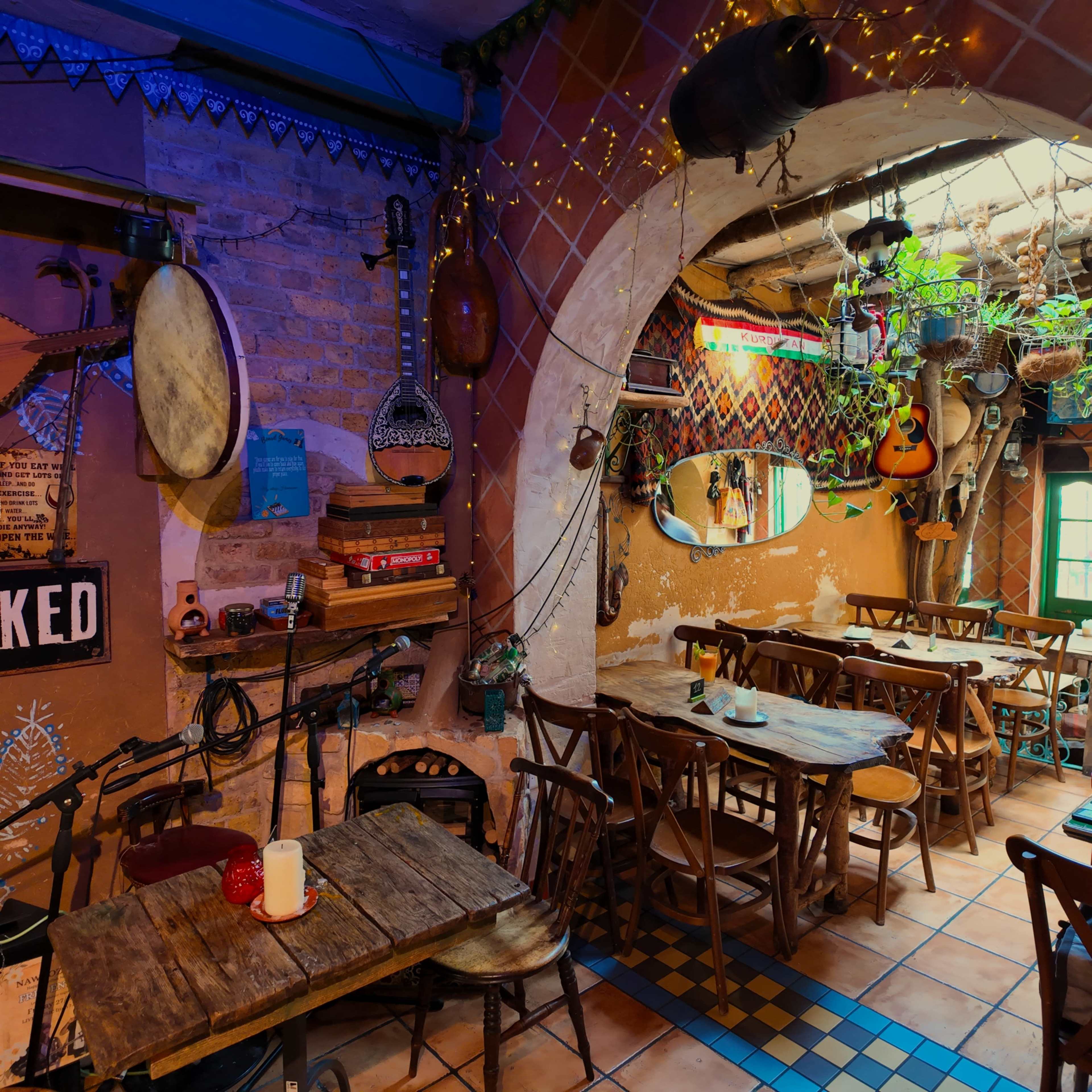 The image shows a cozy restaurant interior with wooden tables, various musical instruments displayed on the walls, and decorative plants hanging from the ceiling.