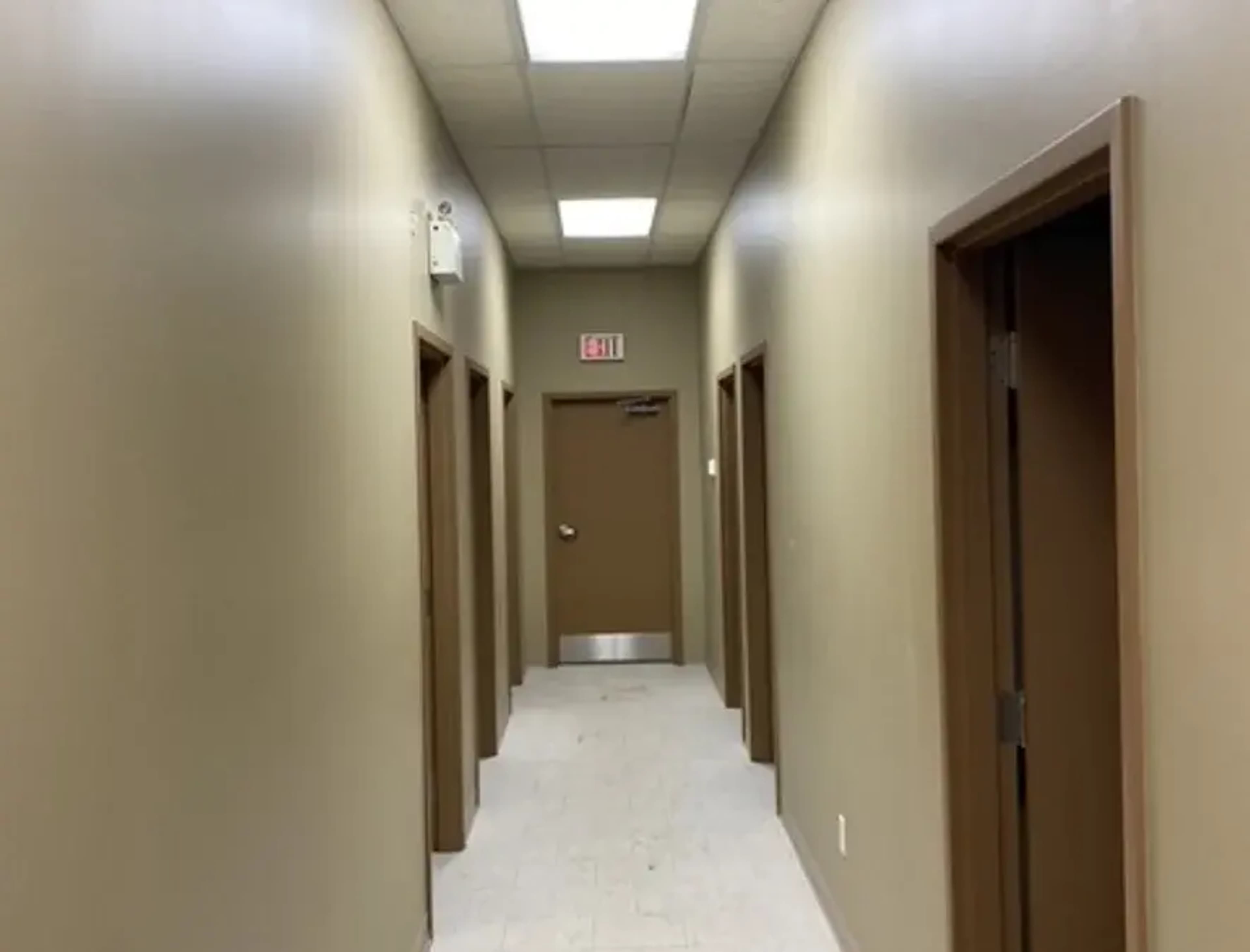 A narrow hallway with several doorways on either side and an exit door at the end.