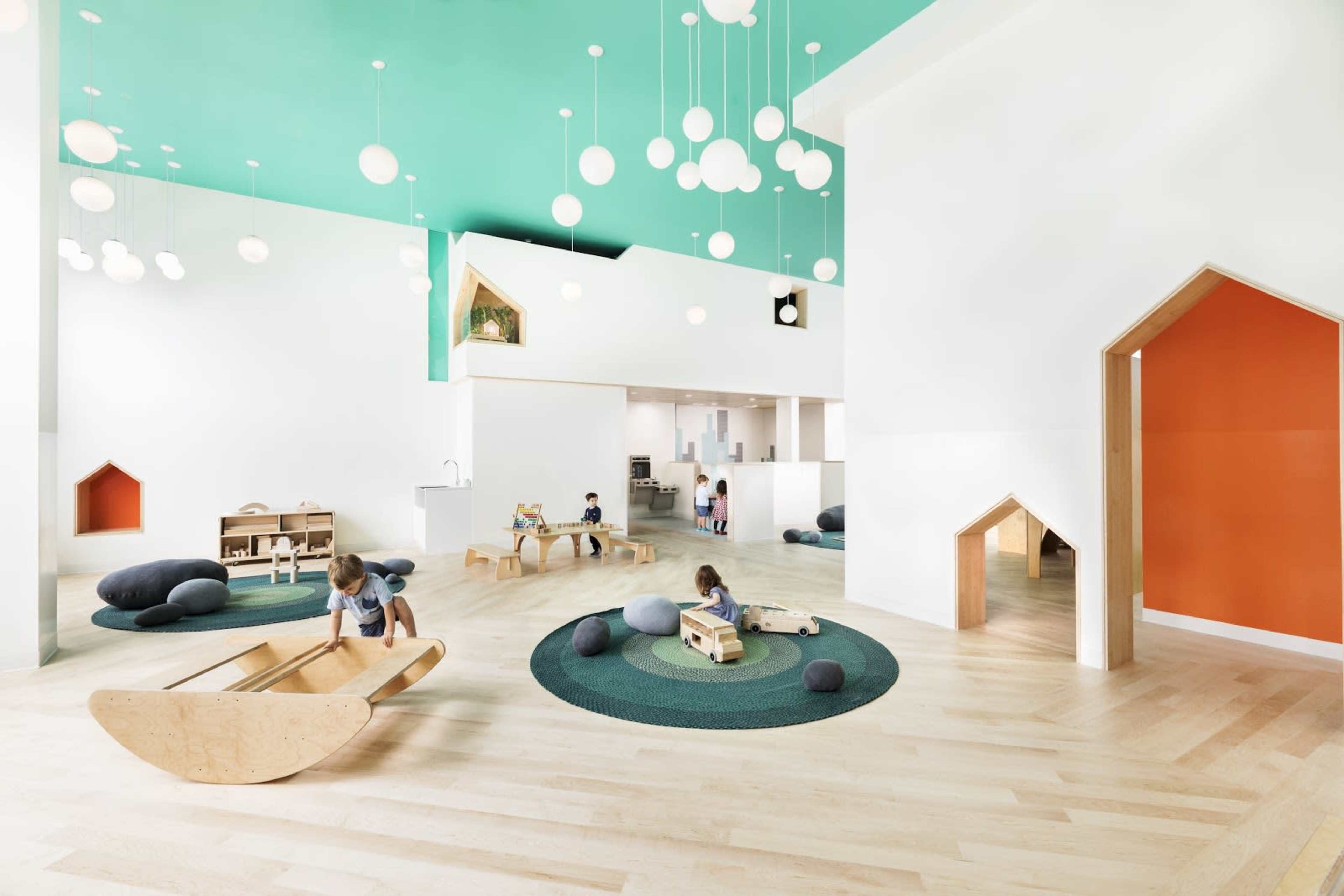 A brightly lit children's play area featuring wooden toys, circular rugs, and whimsical architectural elements.