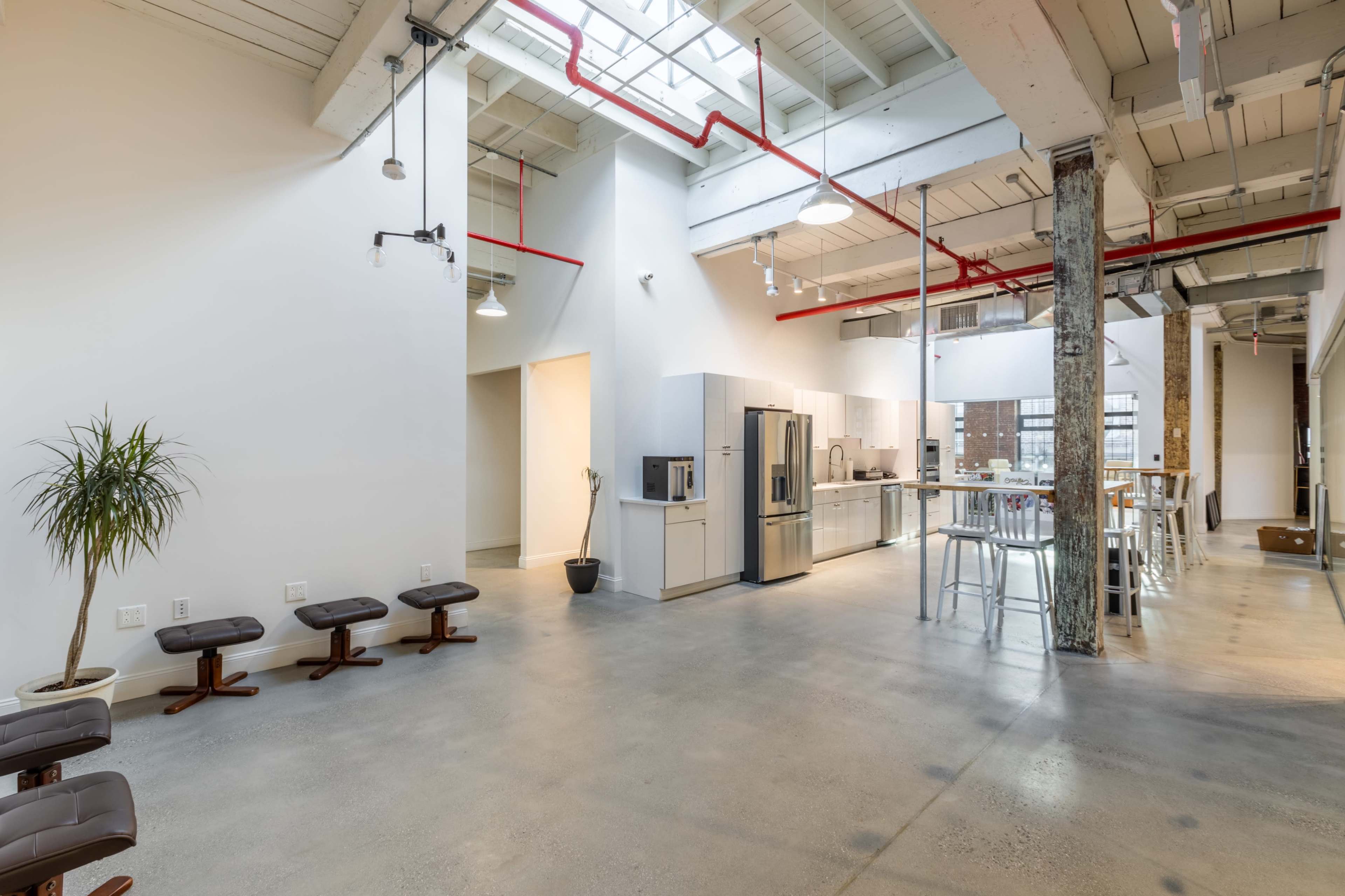 The image shows a spacious, modern industrial-style interior featuring an open kitchen area, tall stools at a counter, and polished concrete floors.