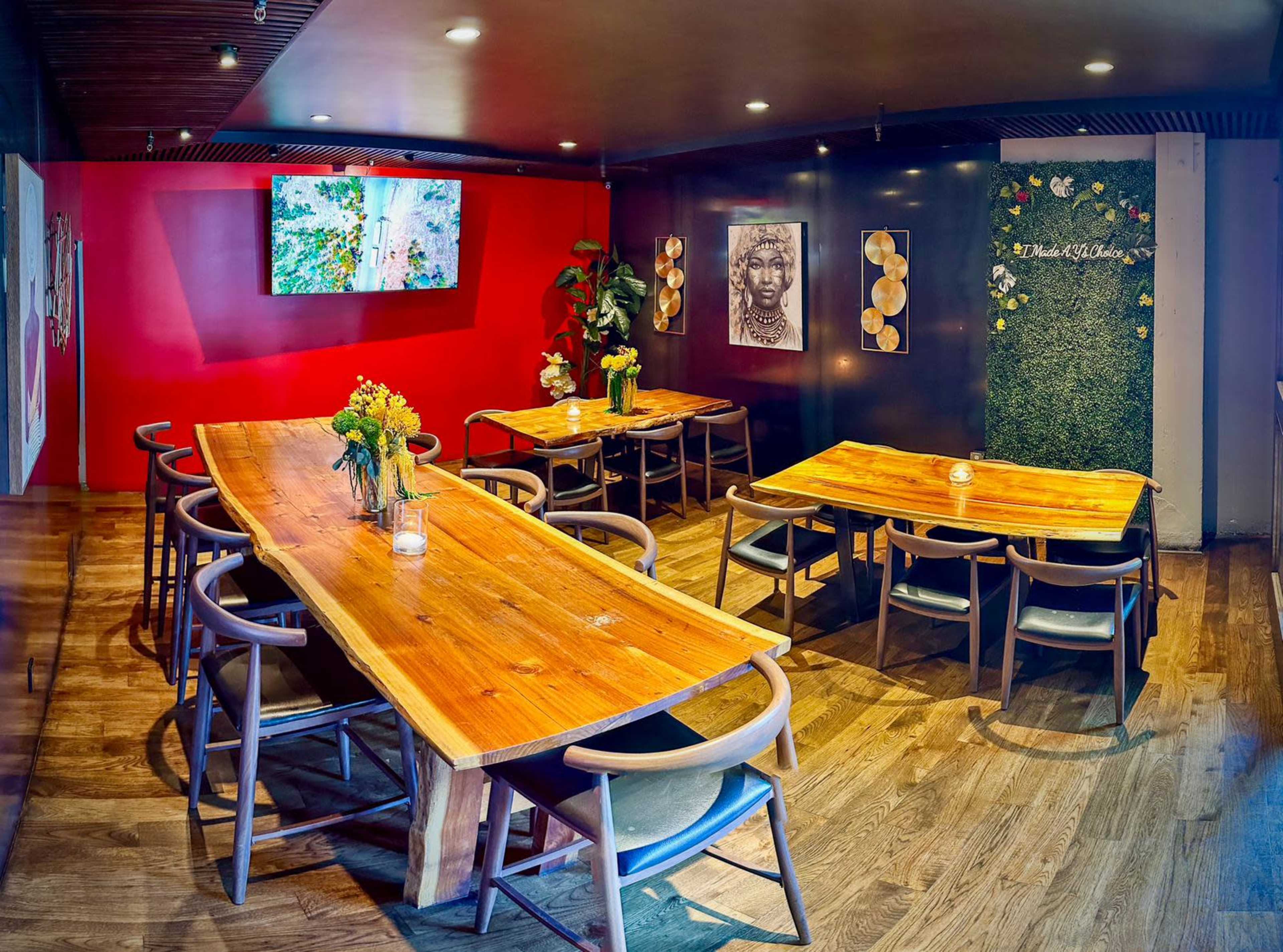 The image shows a restaurant interior featuring wooden tables and chairs, a television on the wall, decorative artwork, and plants.