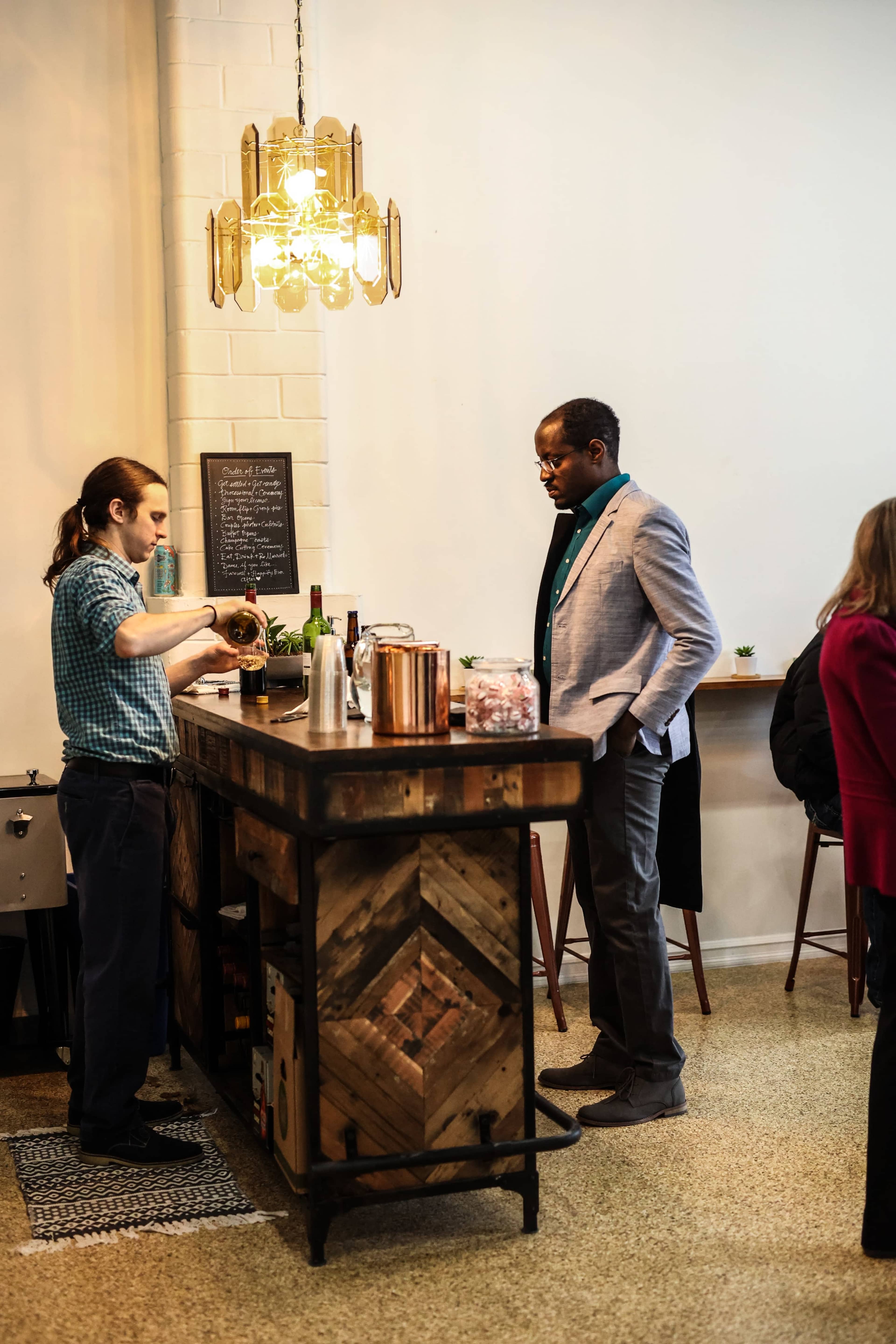 A bartender mixes a drink at a rustic bar while a customer watches in a modern setting.