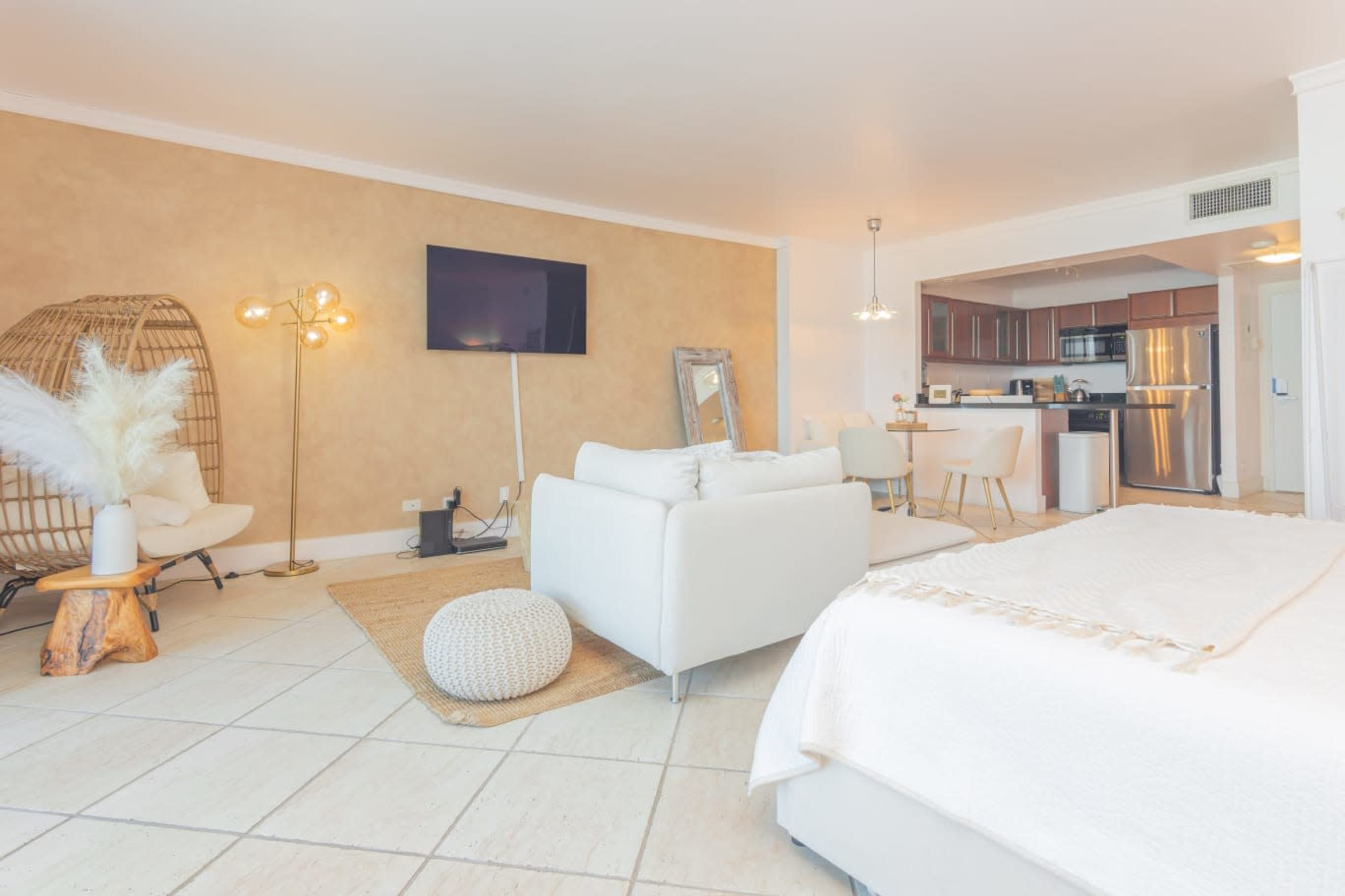 A modern, well-lit open living space featuring a cozy seating area, a kitchen with stainless steel appliances, and a decorative light fixture.