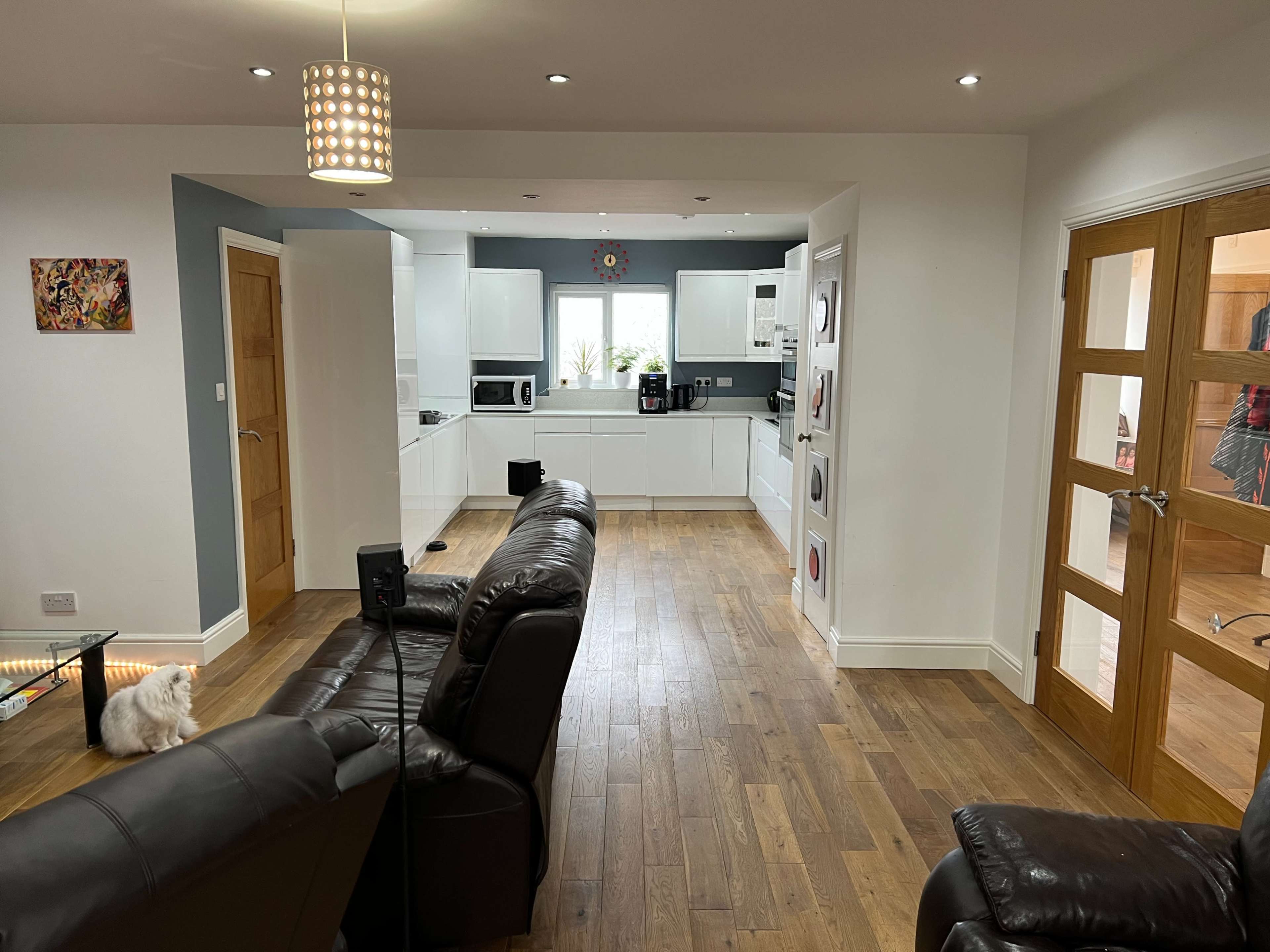 A modern open-plan living area with a kitchen, dining space, and seating area, featuring wooden flooring and light-colored cabinetry.