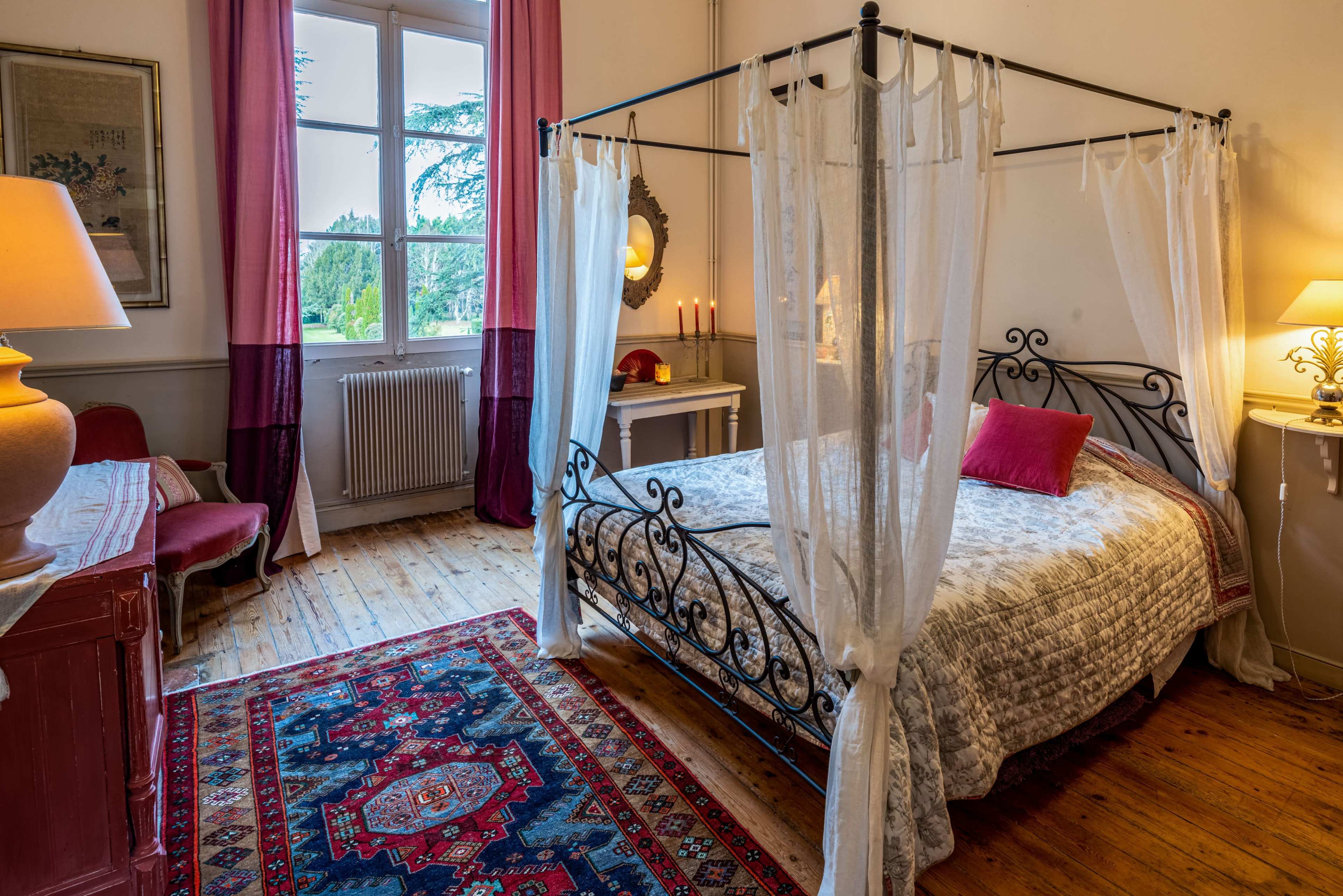The image shows a bedroom with a four-poster bed, a wooden floor, and a large window draped with curtains.
