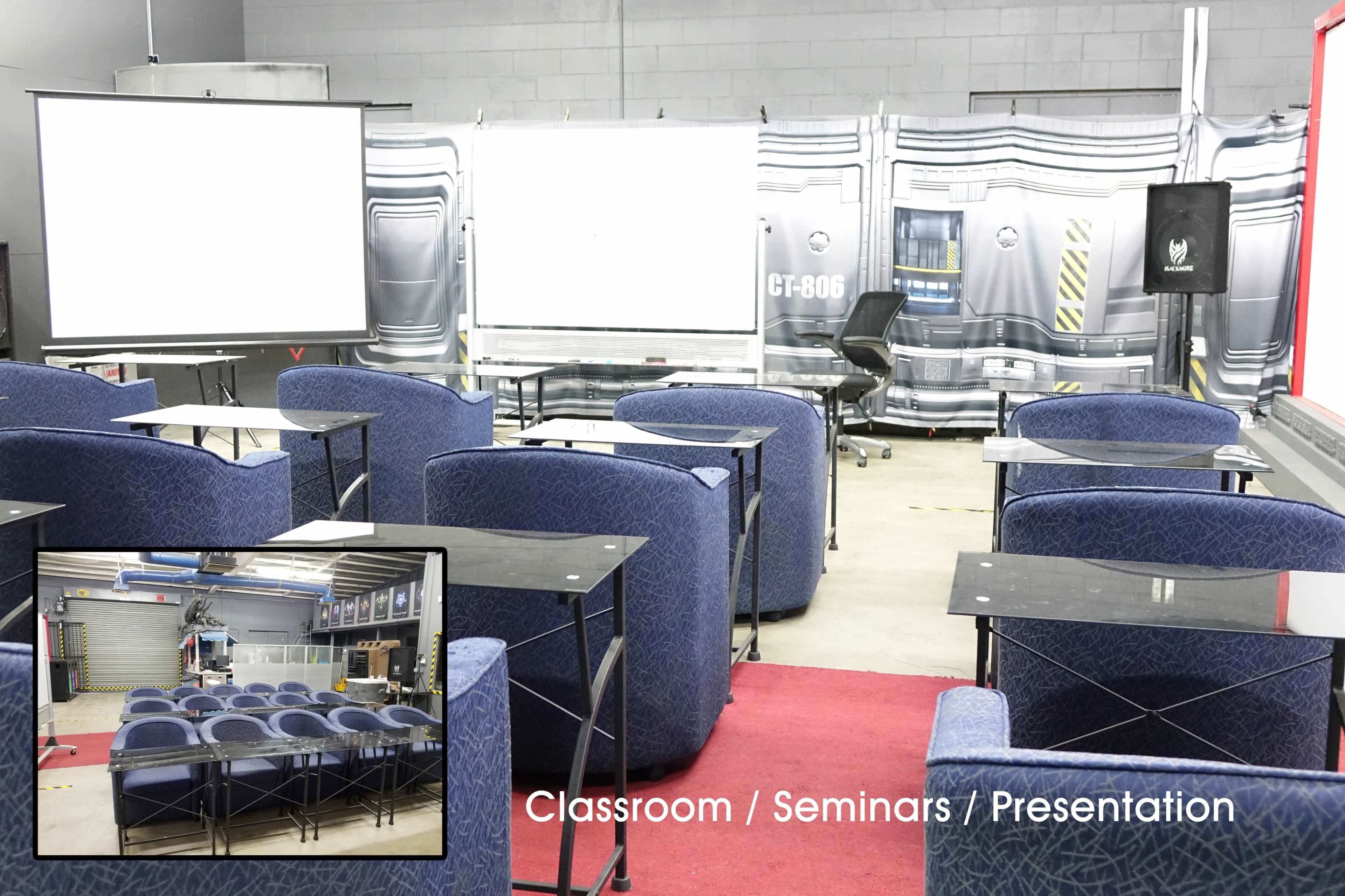 The image shows a furnished seminar room with several chairs arranged in front of whiteboards and a microphone setup against a backdrop.