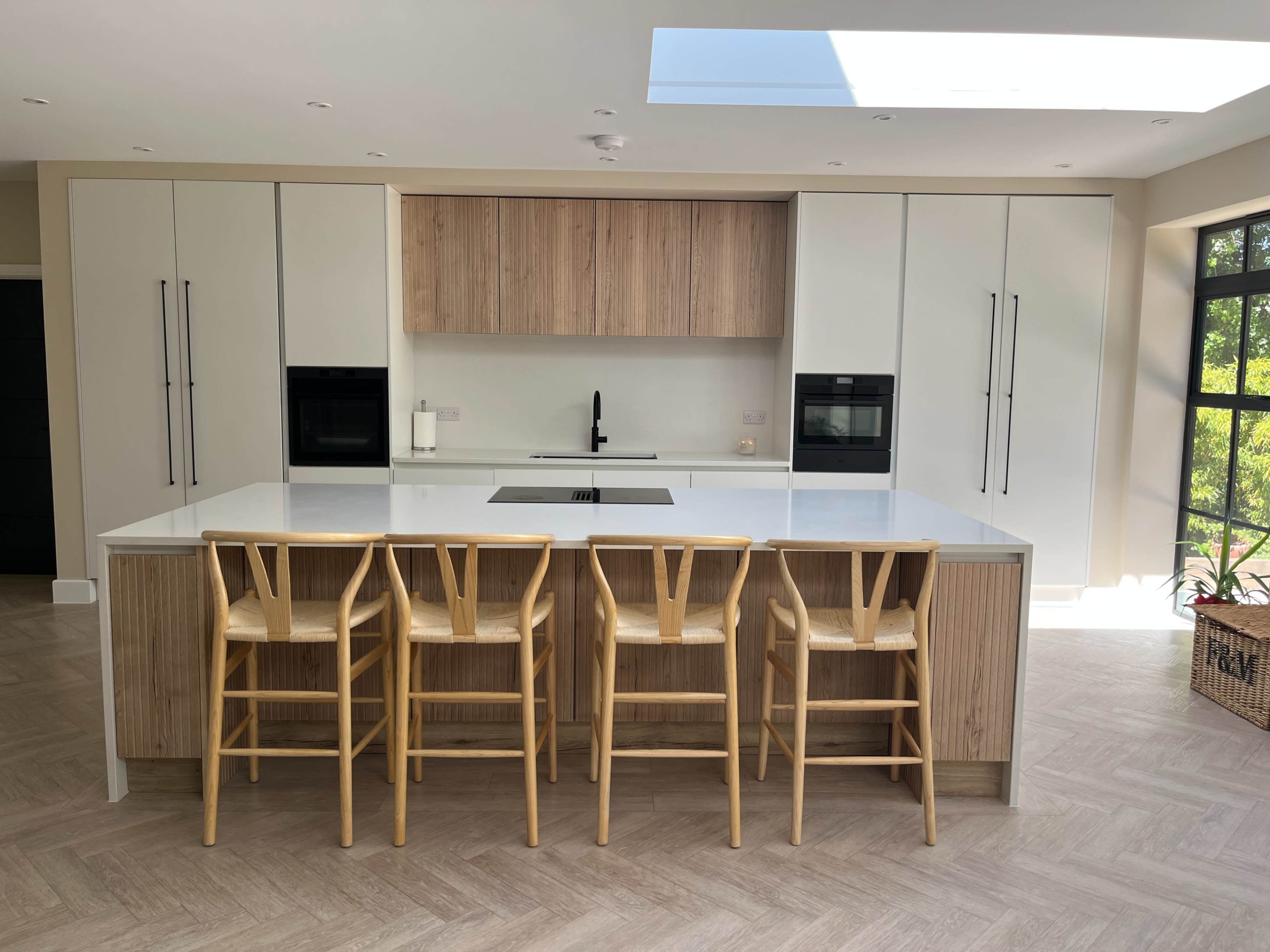 A modern kitchen features a large island with seven wooden barstools, sleek cabinetry, and two built-in ovens.