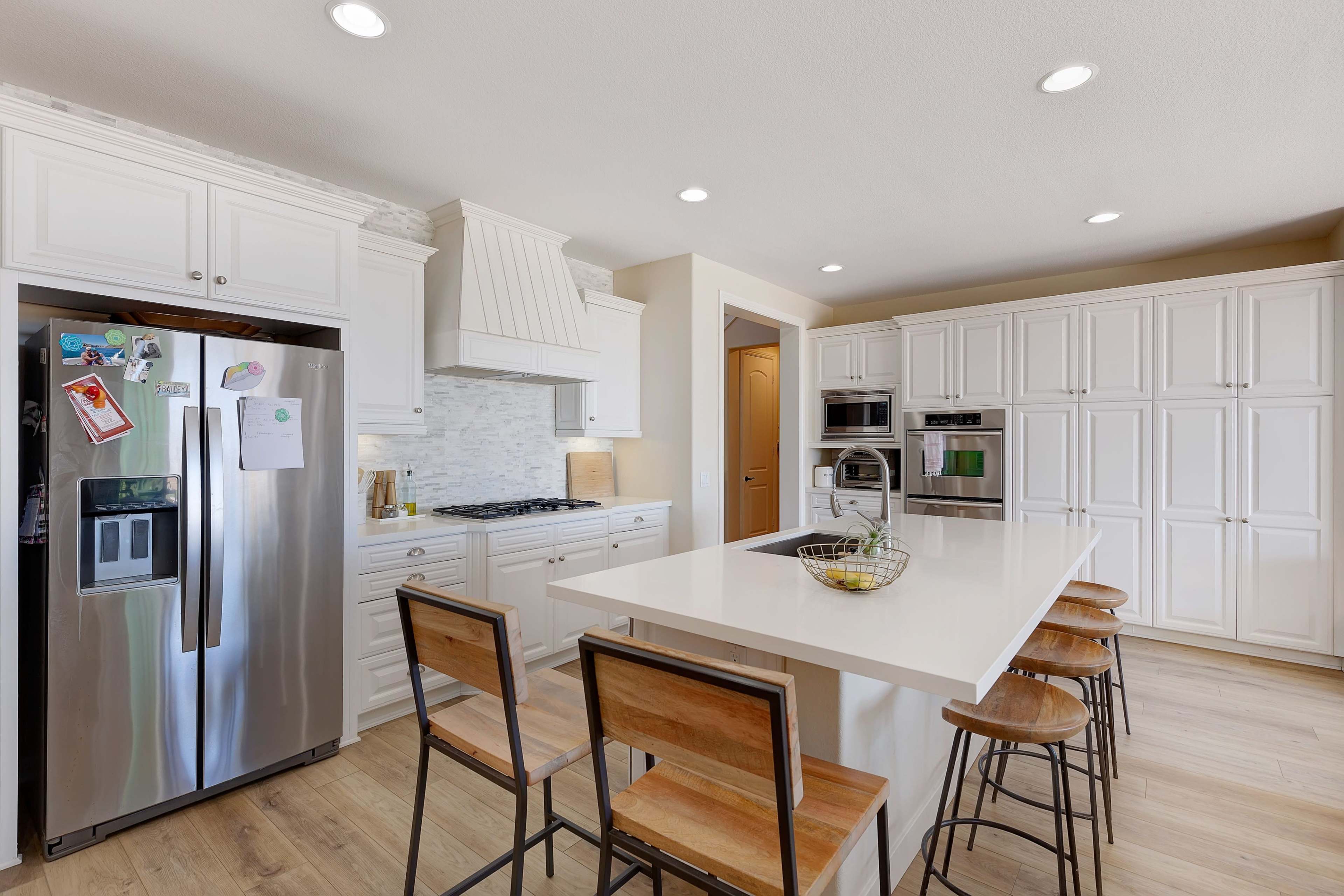 A modern kitchen with white cabinetry, a large island with bar stools, and stainless steel appliances.