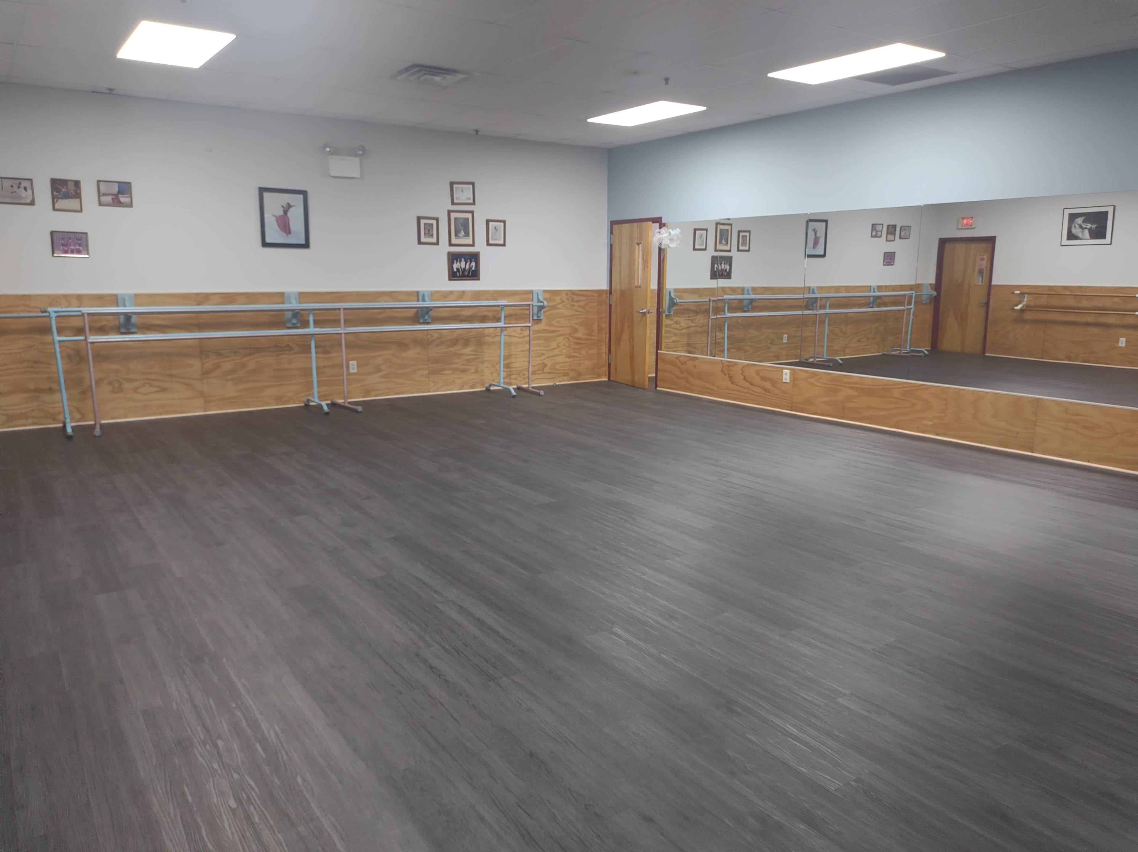 The image shows a spacious dance studio with wooden walls, a mirrored wall, and ballet barres along the sides.