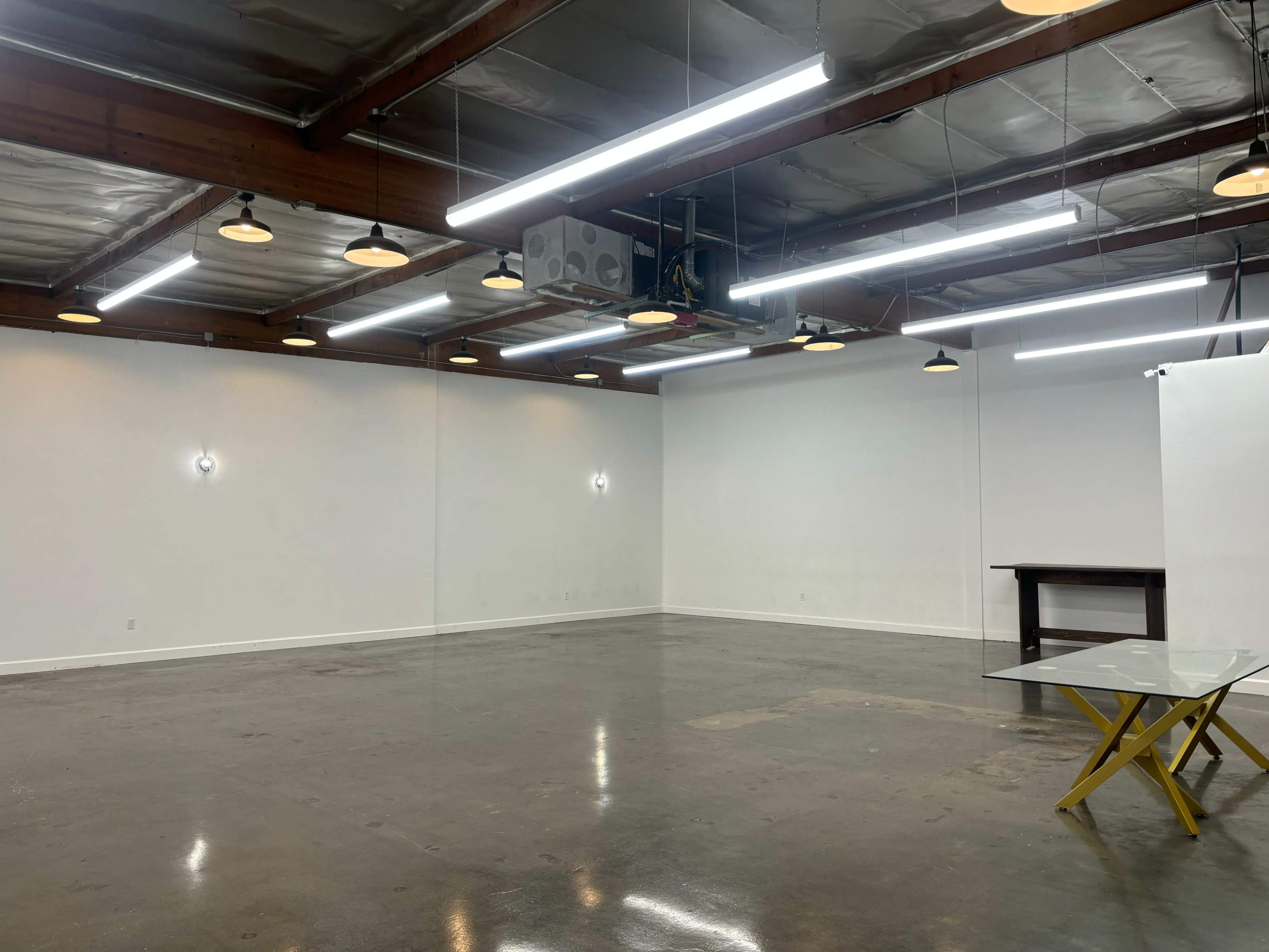 The image shows an empty industrial-style interior space with polished concrete floors, white walls, and overhead lighting.