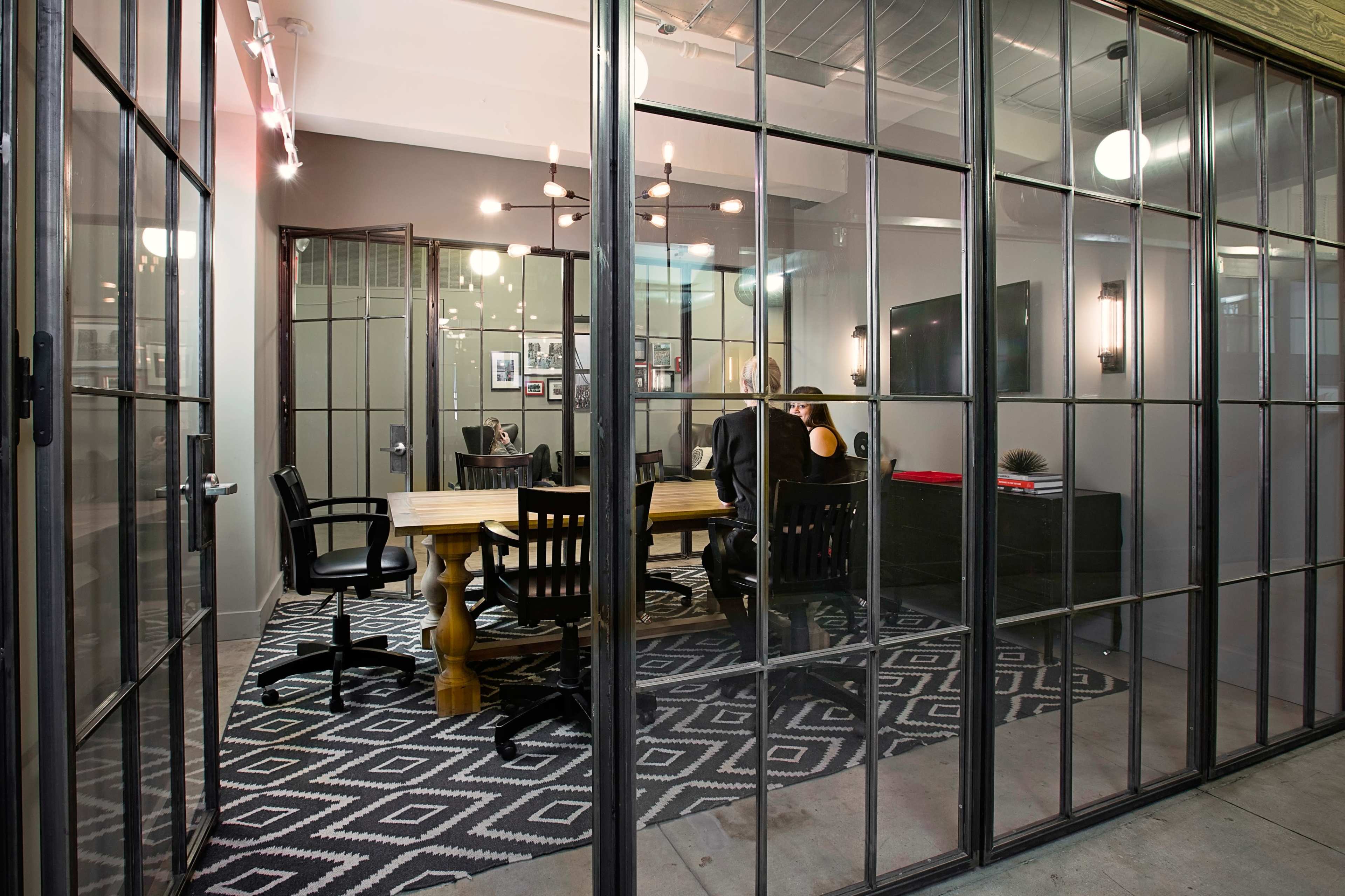 A conference room with a large wooden table and black chairs is visible through glass-paneled walls.