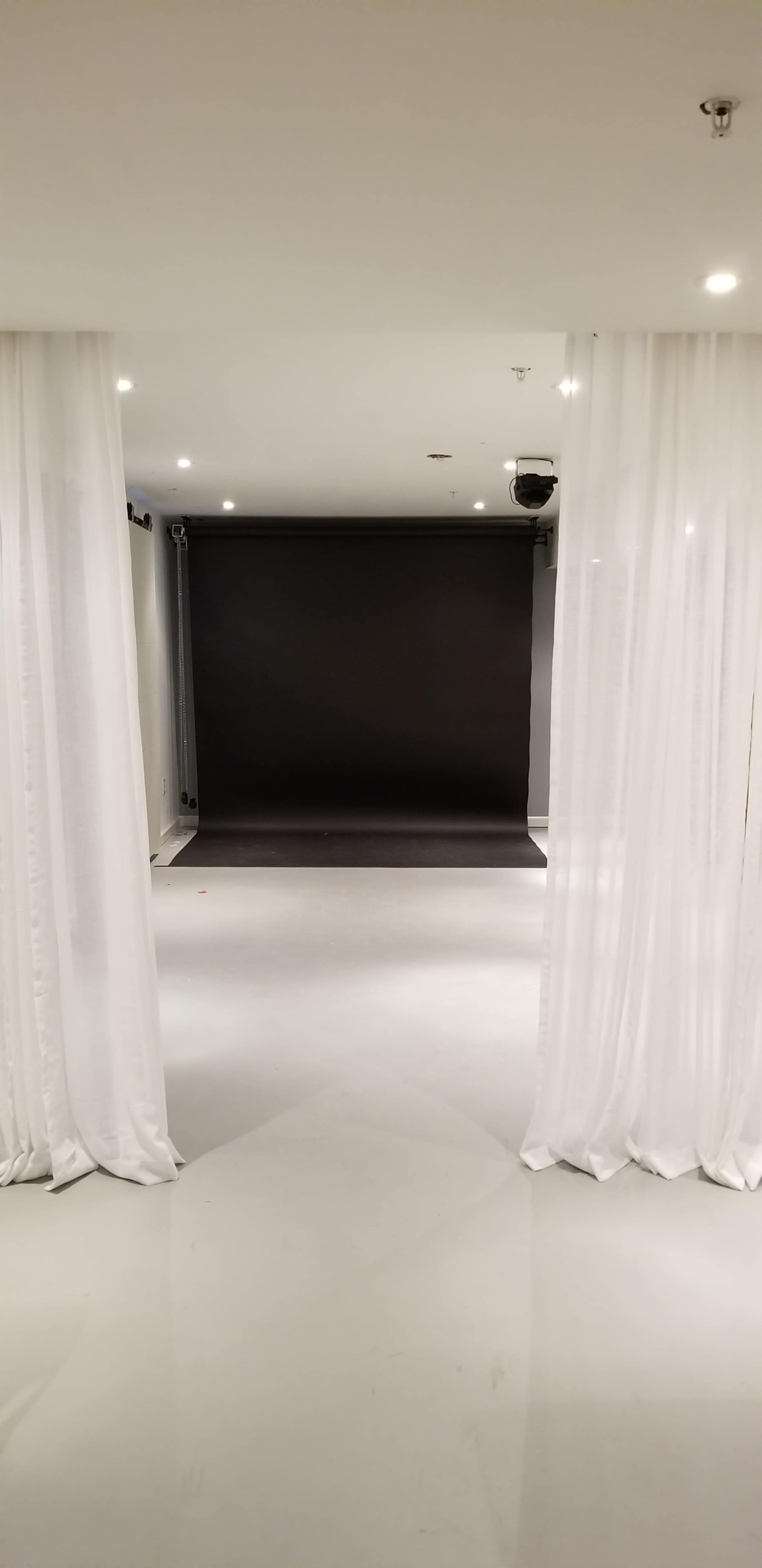 A spacious studio with white curtains framing a dark backdrop and a well-lit floor.