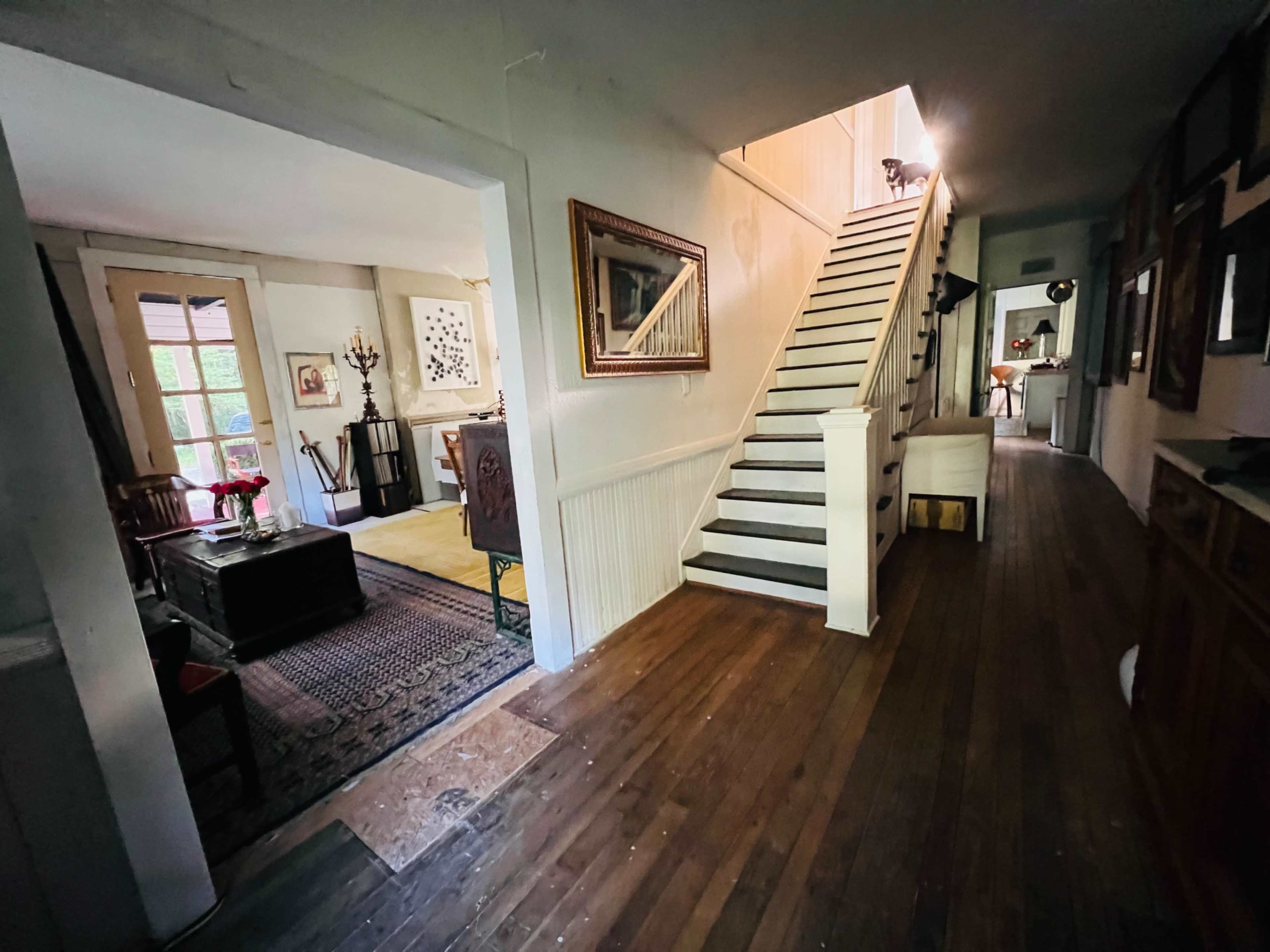 The image shows a hallway leading to a staircase, with rooms visible on either side and wooden flooring throughout.